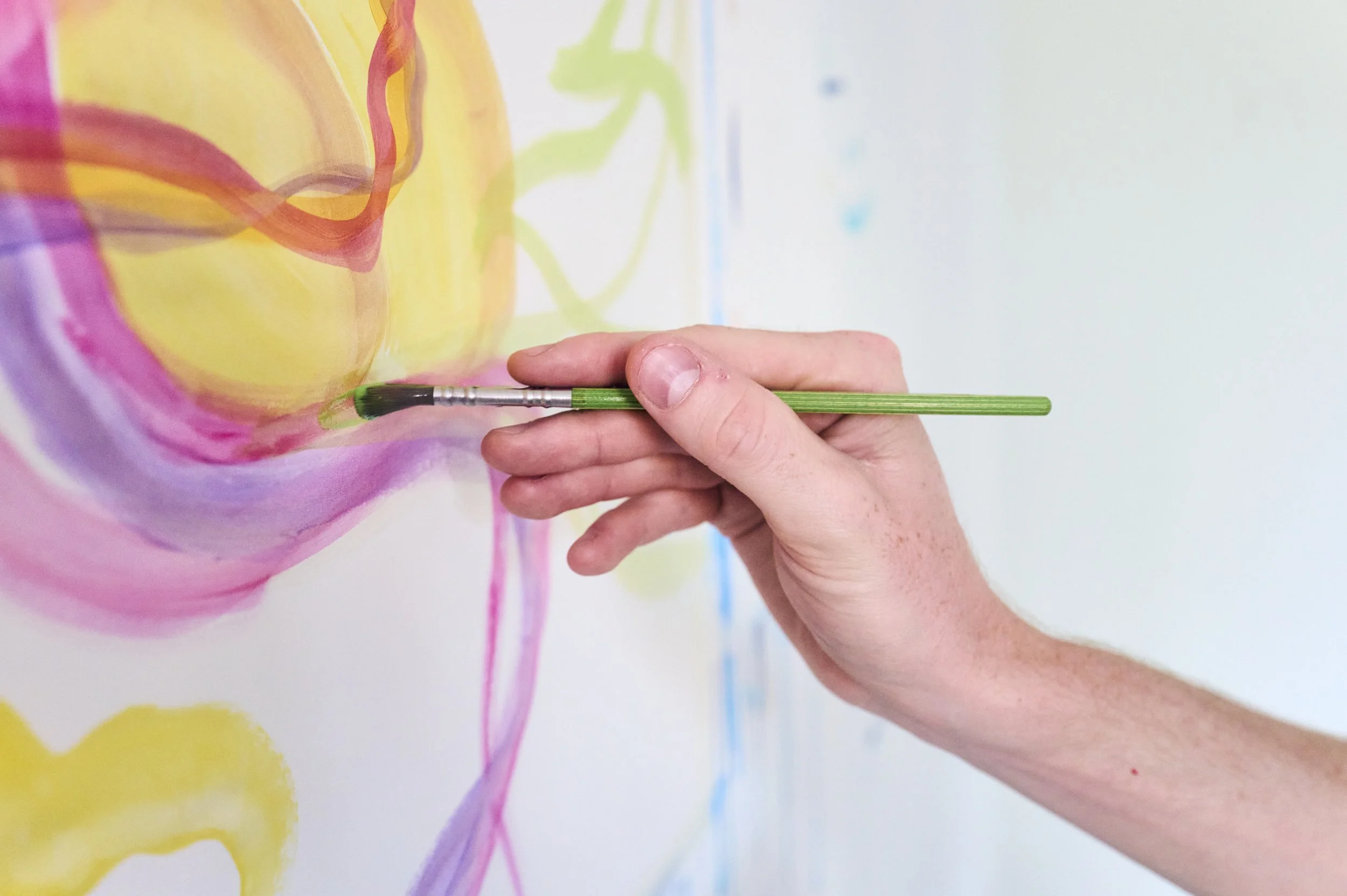 Hand mit Pinsel trägt bunte Farben auf eine weisse Wand auf