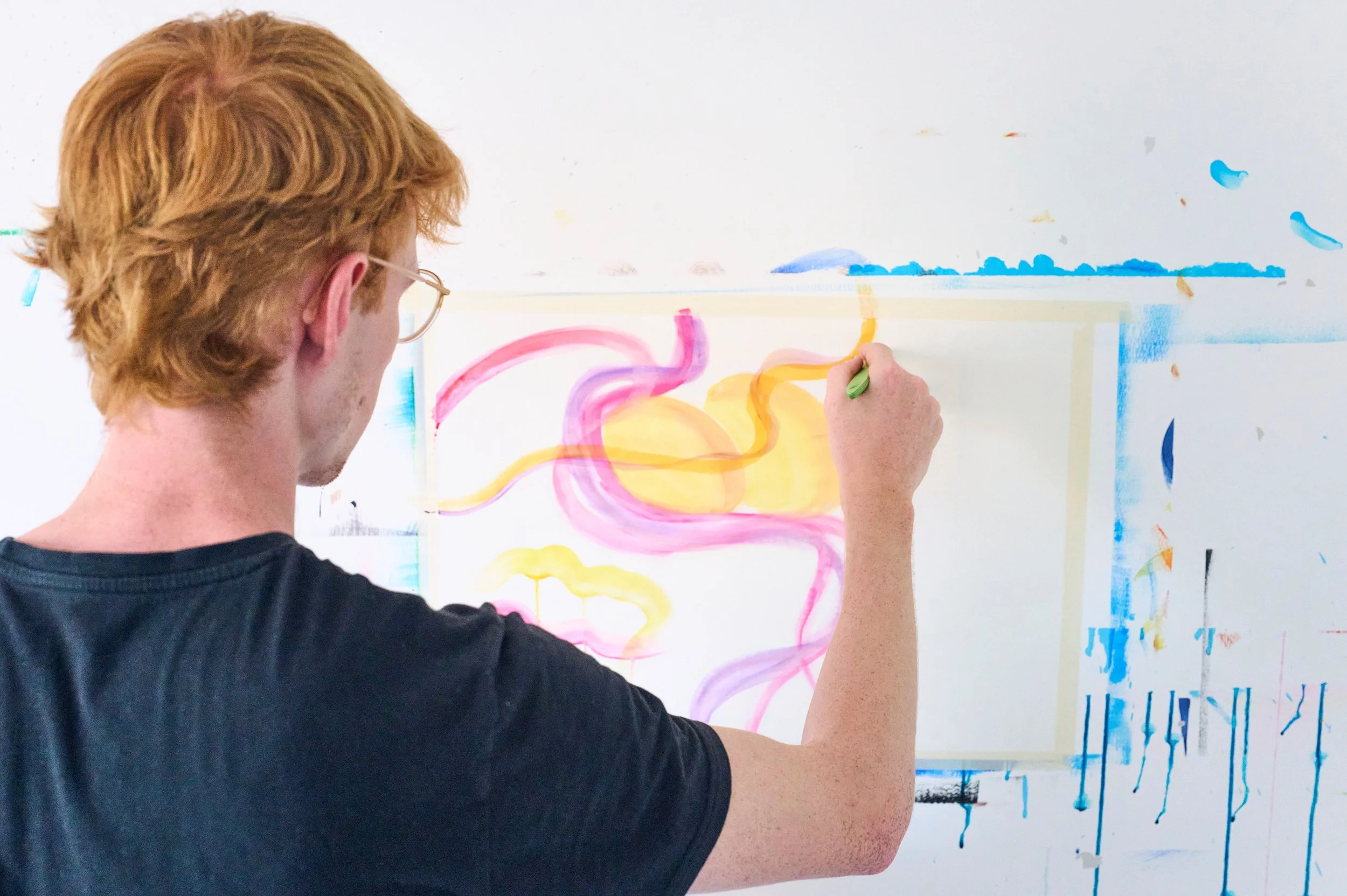 Mann malt mit dem Pinsel bunte Formen auf eine weisse Wand während einer Kunsttherapiestunde
