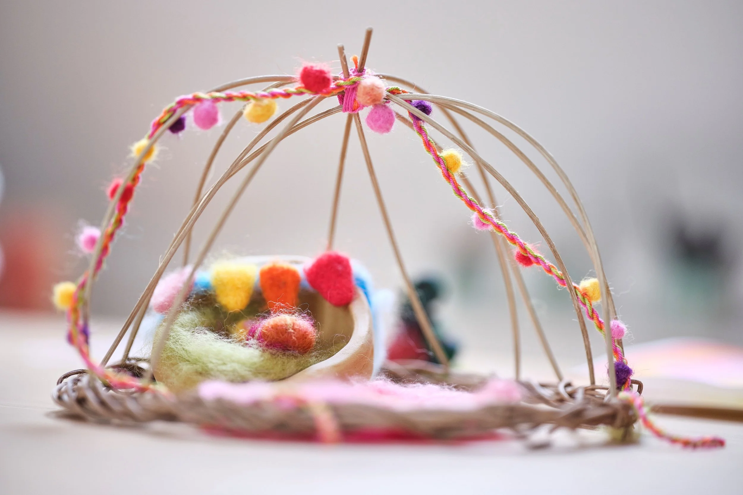 Nest mit Filzpüppchen und einem Bogen aus bunten Wollfäden, Kunstwerk aus einer Therapiestunde