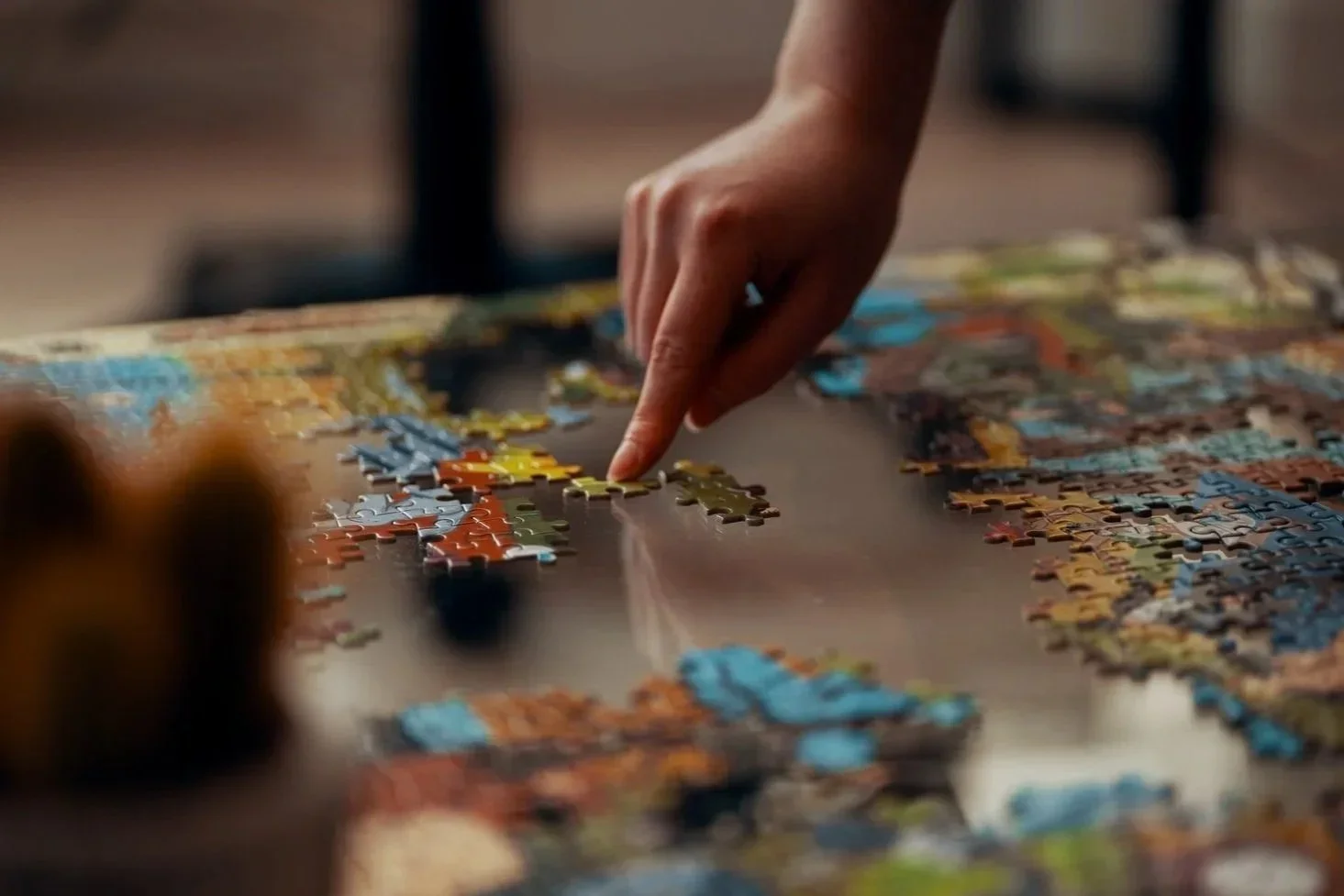 A person assembling a colorful jigsaw puzzle on a table.
