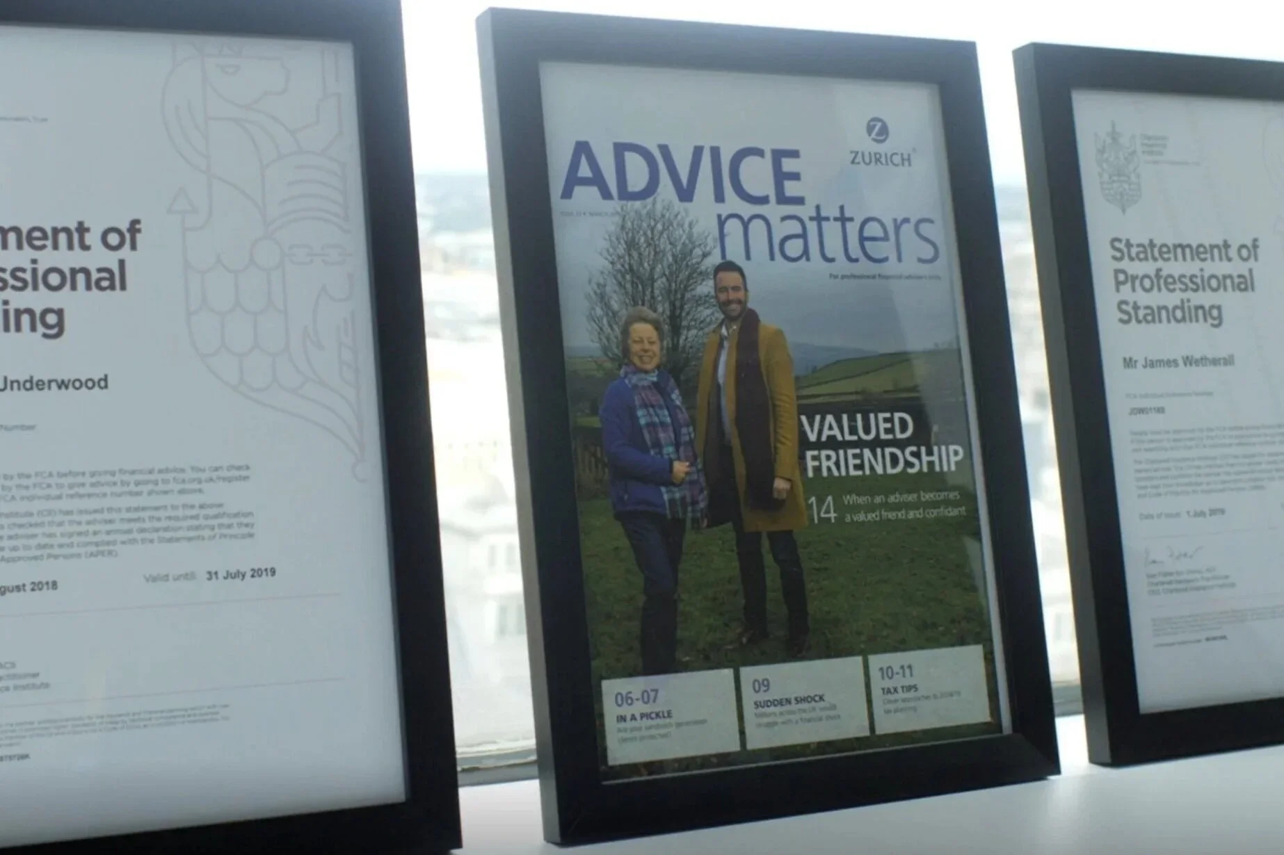 Three framed posters on display, with the middle poster showing a man and a woman smiling outdoors. The middle poster has the words "ADVICE matters" at the top and "VALUED FRIENDSHIP" at the bottom, along with small text and icons at the bottom. The left and right posters contain text about professional standing and certification.