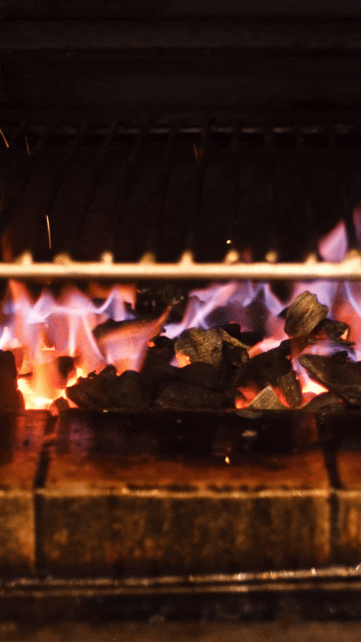 Gros plan sur un barbecue avec du charbon de bois qui brûle et des flammes.