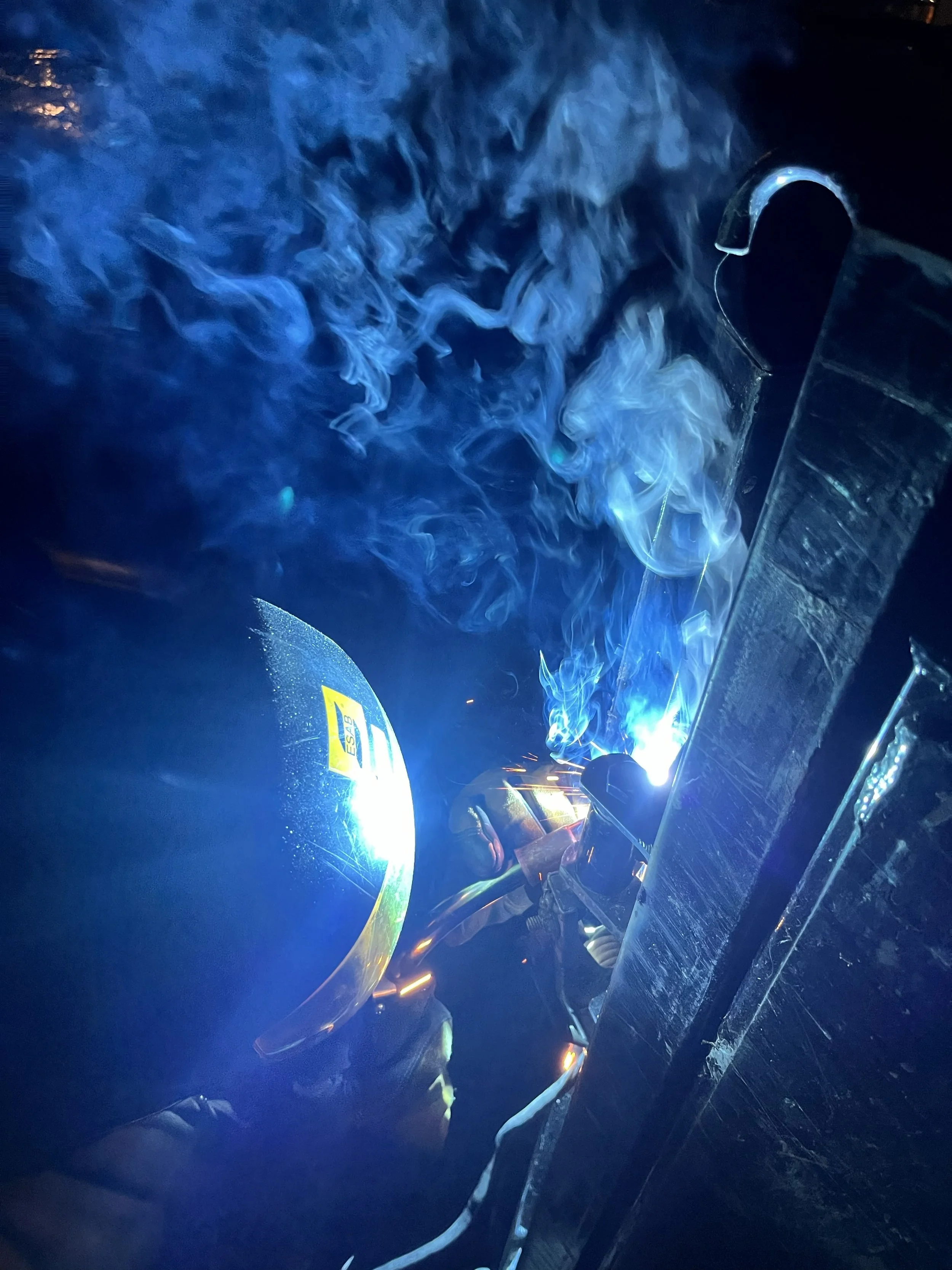 A person welding metal, with bright sparks and blue smoke in a dark setting.