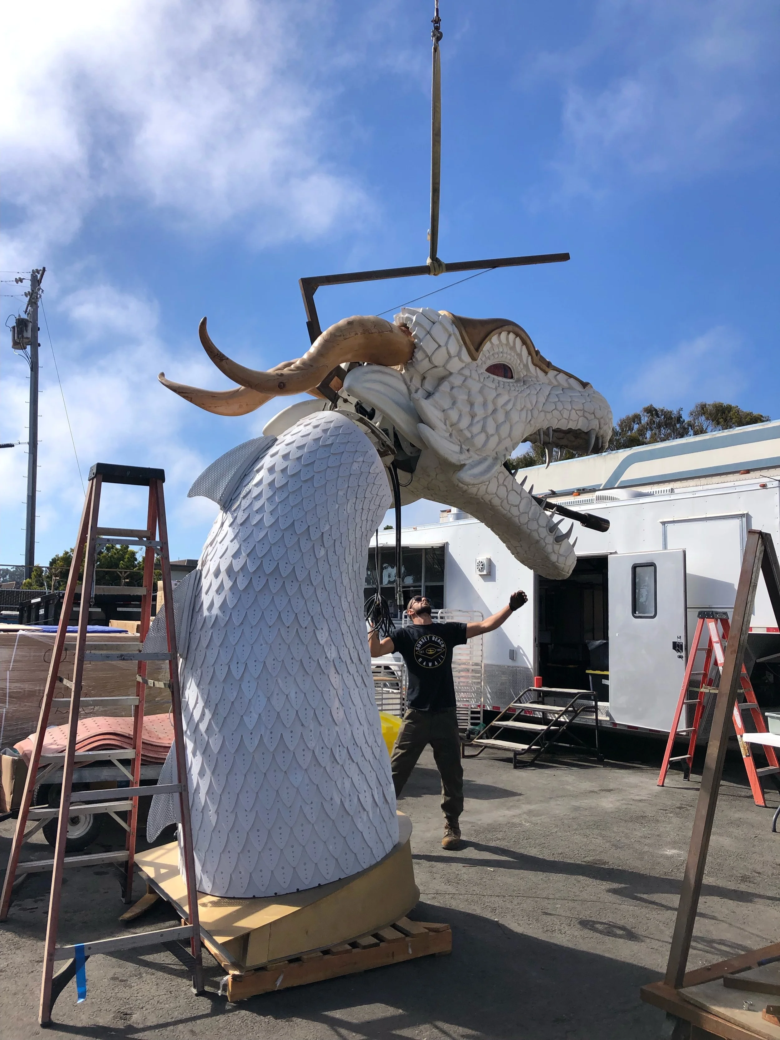 A person standing outdoors in front of a large white dragon statue with scales and horns, with a building and equipment around.