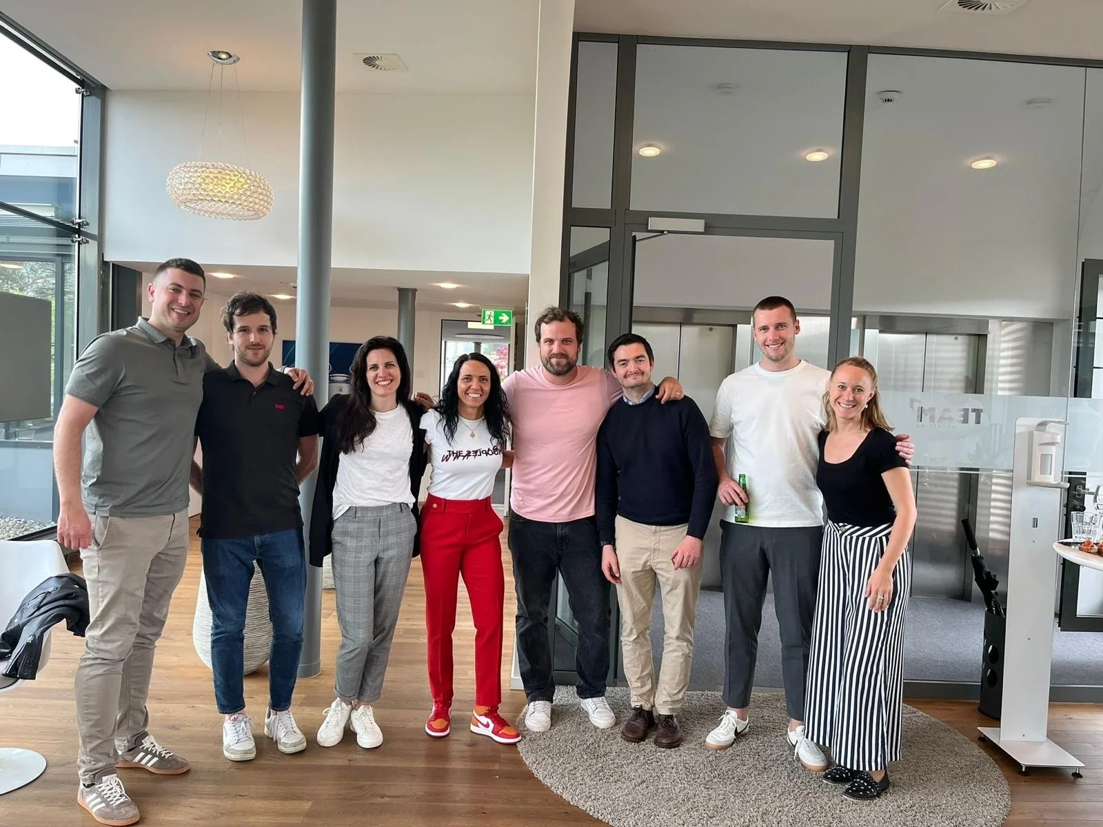 A group of nine people standing together in an indoor setting, smiling and posing for the photo.