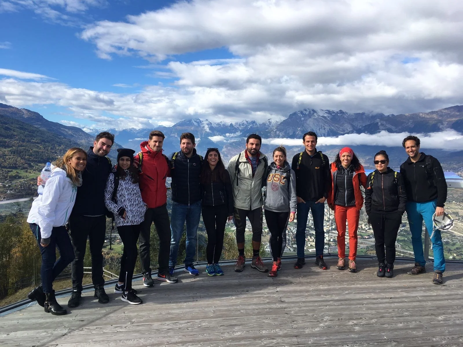 Group of eleven people posing outdoors with mountains and cloudy sky in the background.