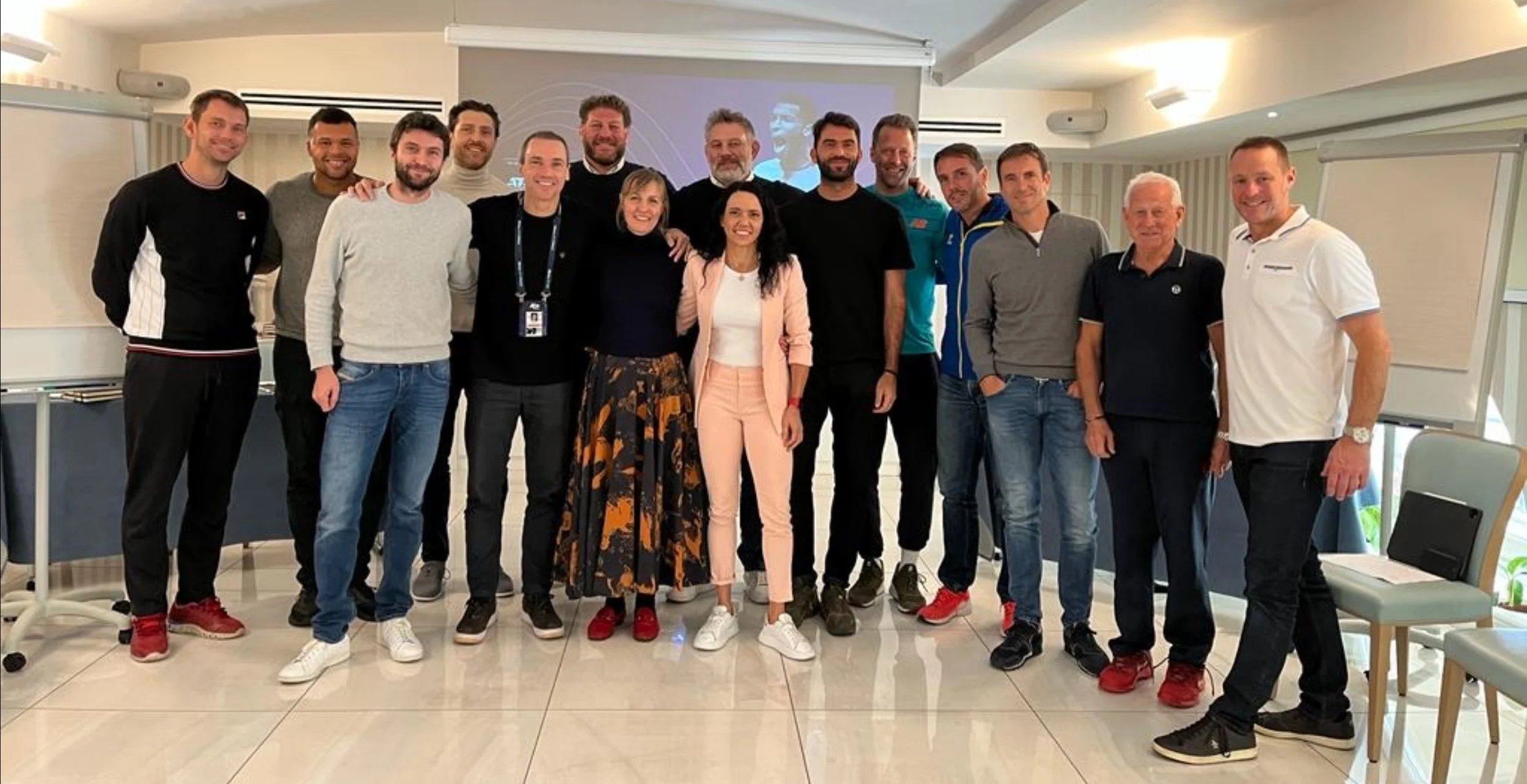 A group of 16 people standing together in a room, smiling for a group photo. There are both men and women, and they appear to be at a professional or conference event.