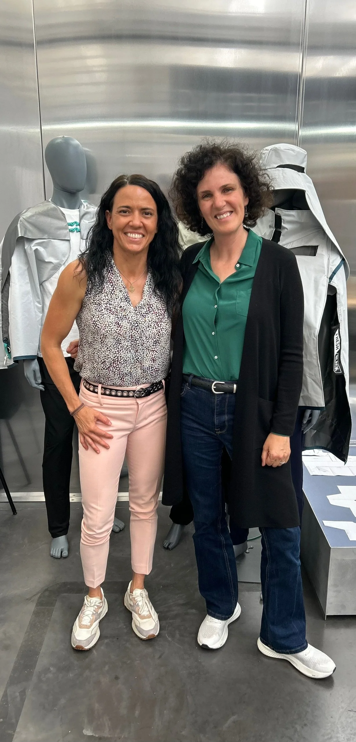 Two women standing side by side in a retail store, smiling, with mannequins wearing outdoor clothing in the background.