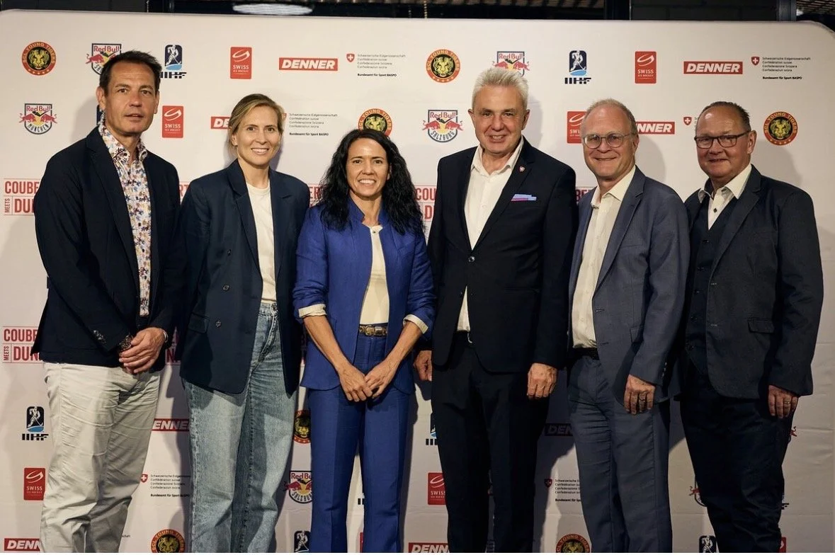 Seven people standing in front of a backdrop with various logos, including Red Bull, Swiss, Denner, and others, at an event or press conference.