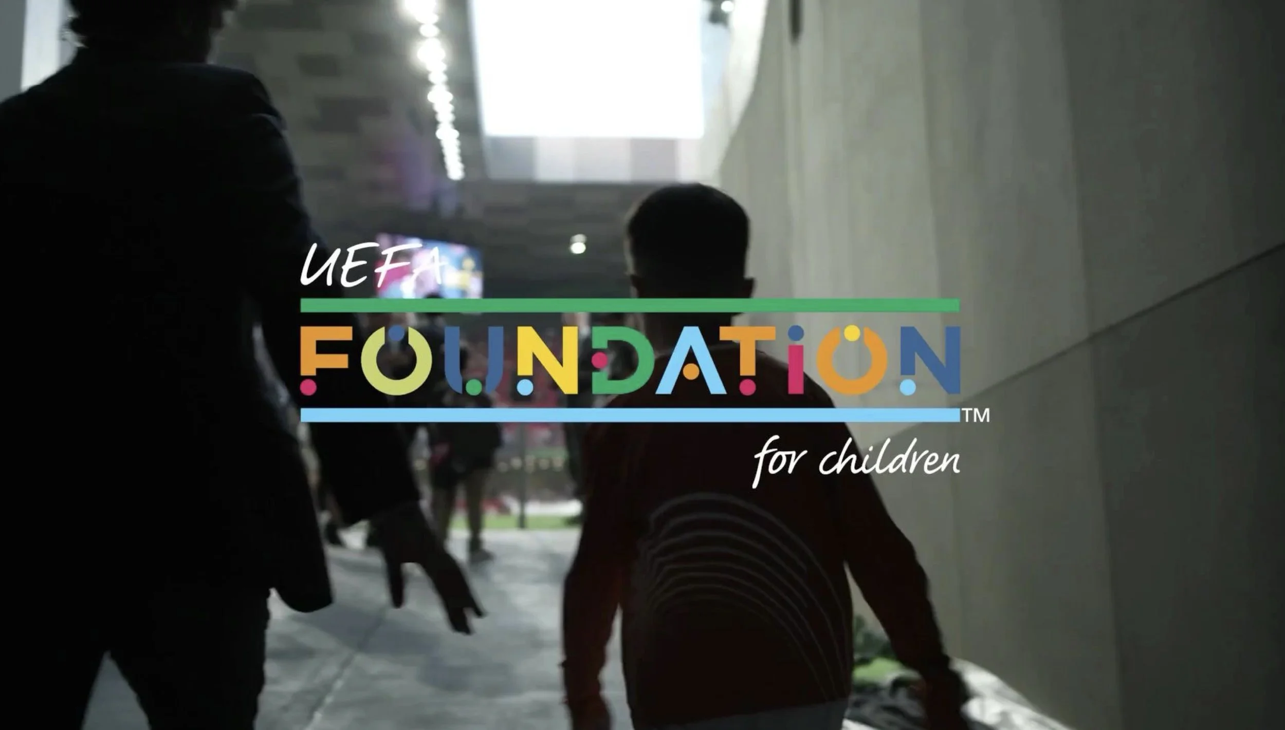 Silhouettes of children holding hands walking through an indoor corridor with bright light at the end, with the logo and text 'UEFA Foundation for children' overlaid.