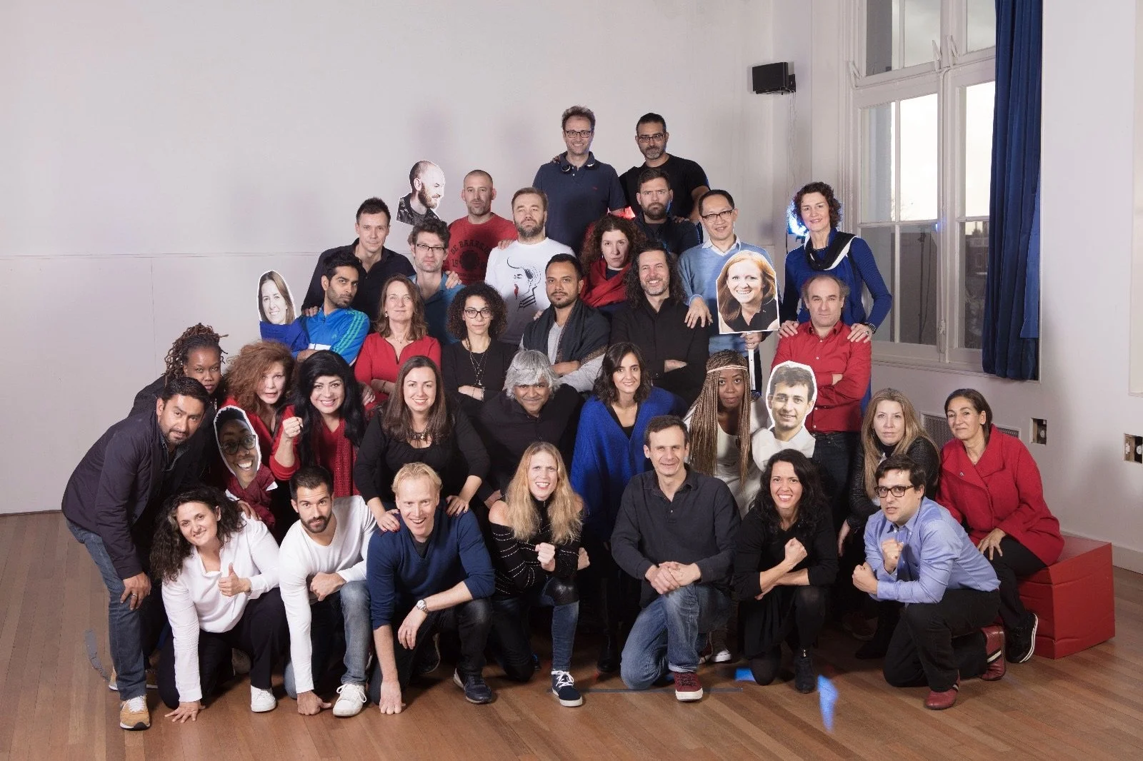Group of diverse people posing together in a room, some holding posters or pictures, celebrating or attending an event.