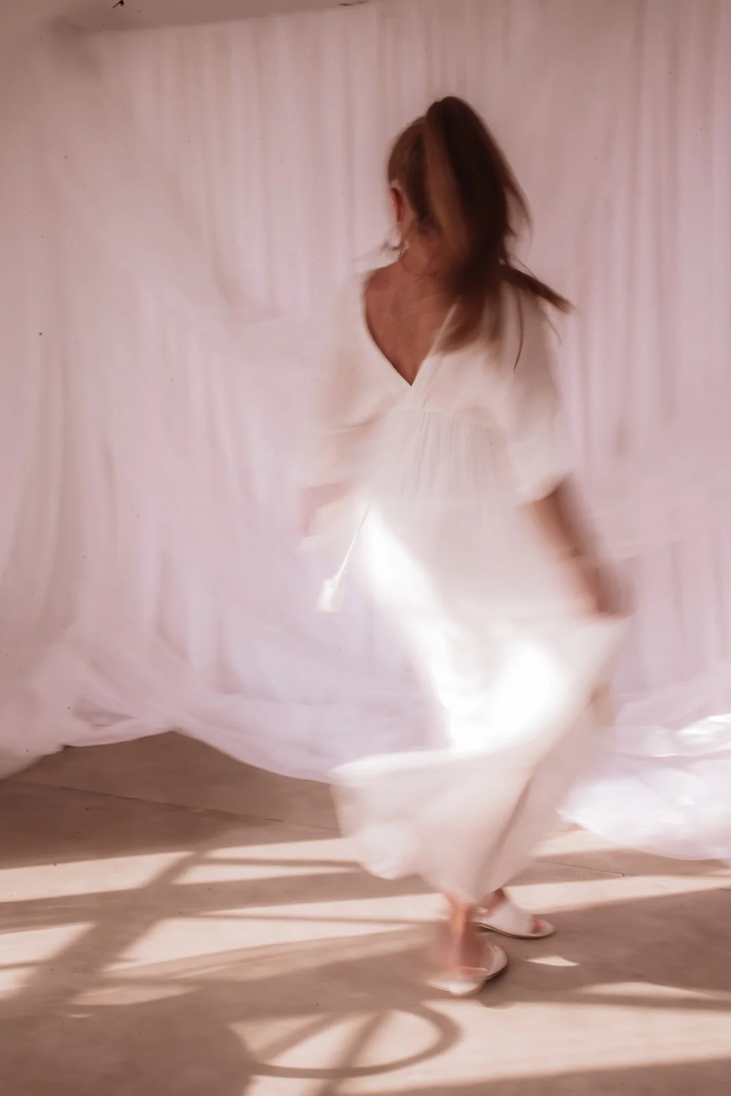 A woman spinning in a white flowing dress, with light filtering through the fabric, creating a soft, dreamy atmosphere.