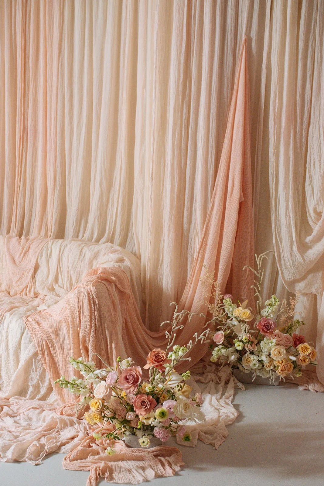 Soft pink and cream drapery with floral arrangements, creating a romantic setting.
