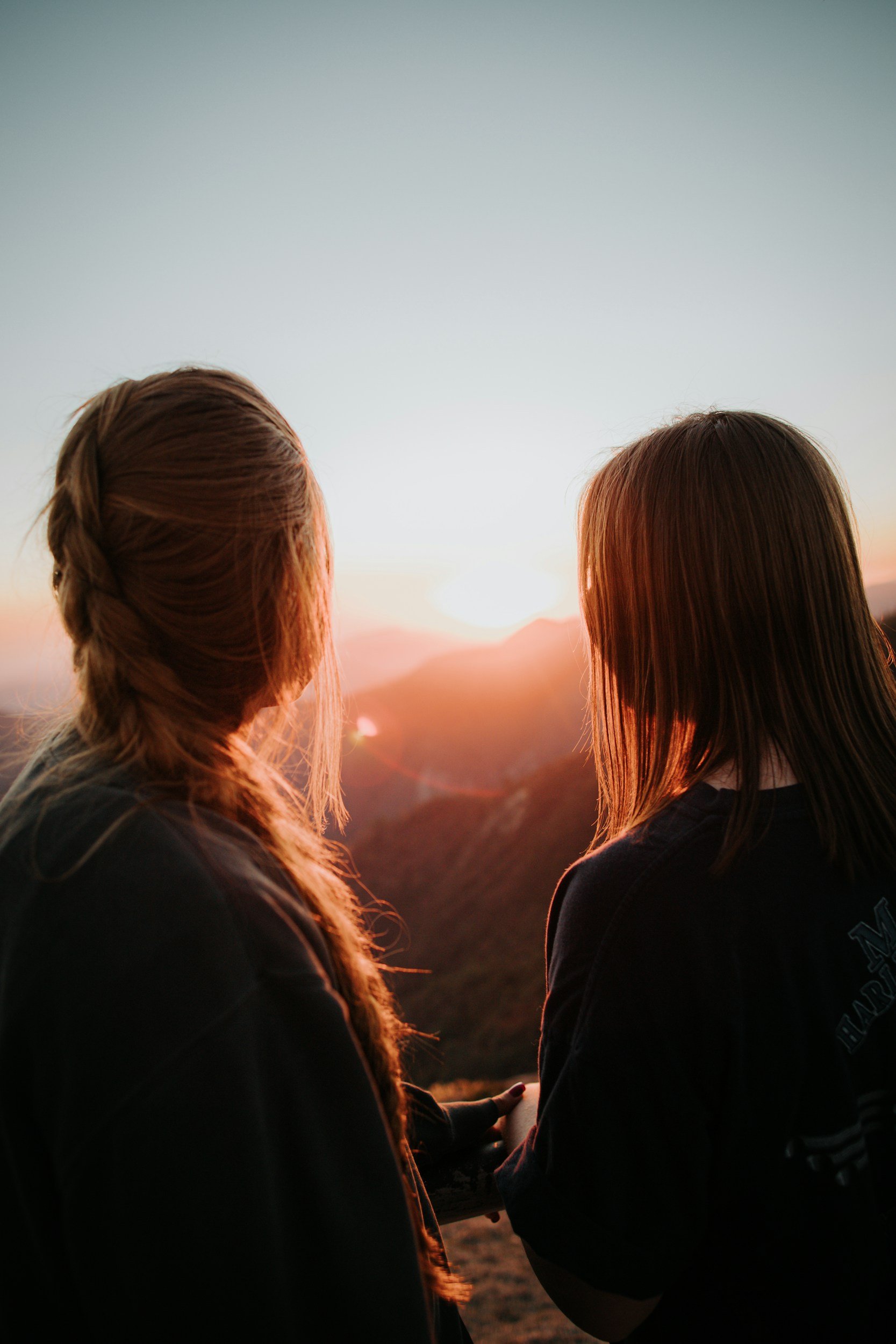 Two women standing side by side looking towards a sunset