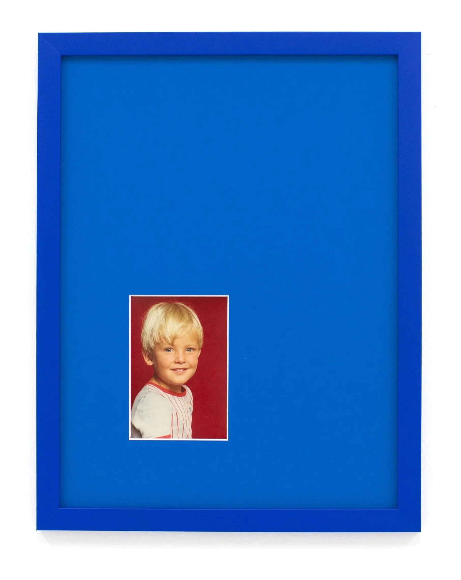 Blue photo frame mounted on a white wall with a portrait of a smiling young boy with blonde hair and blue eyes inside.