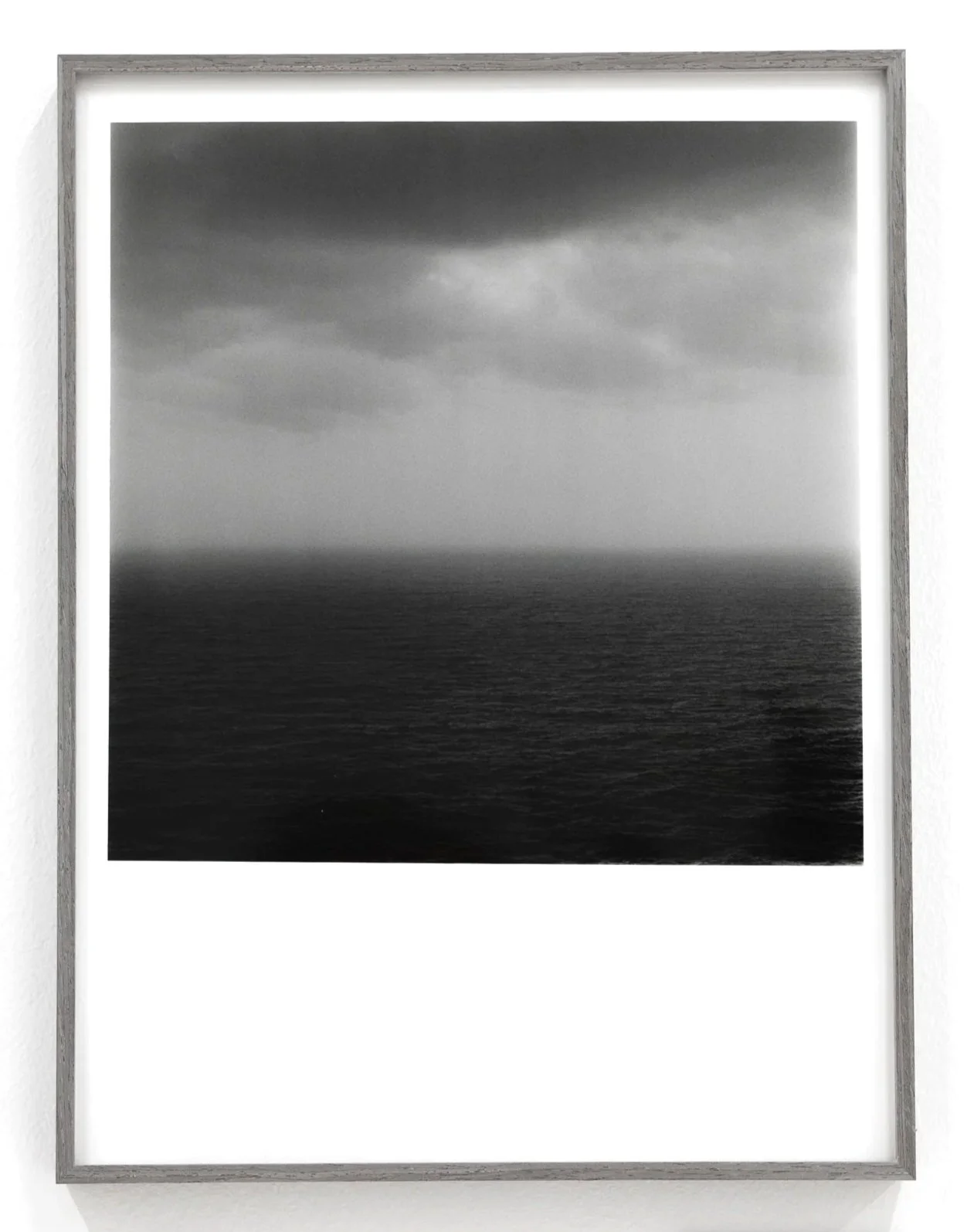 Black and white photograph of a stormy seascape with dark, turbulent clouds against a gray sky and a choppy ocean below.