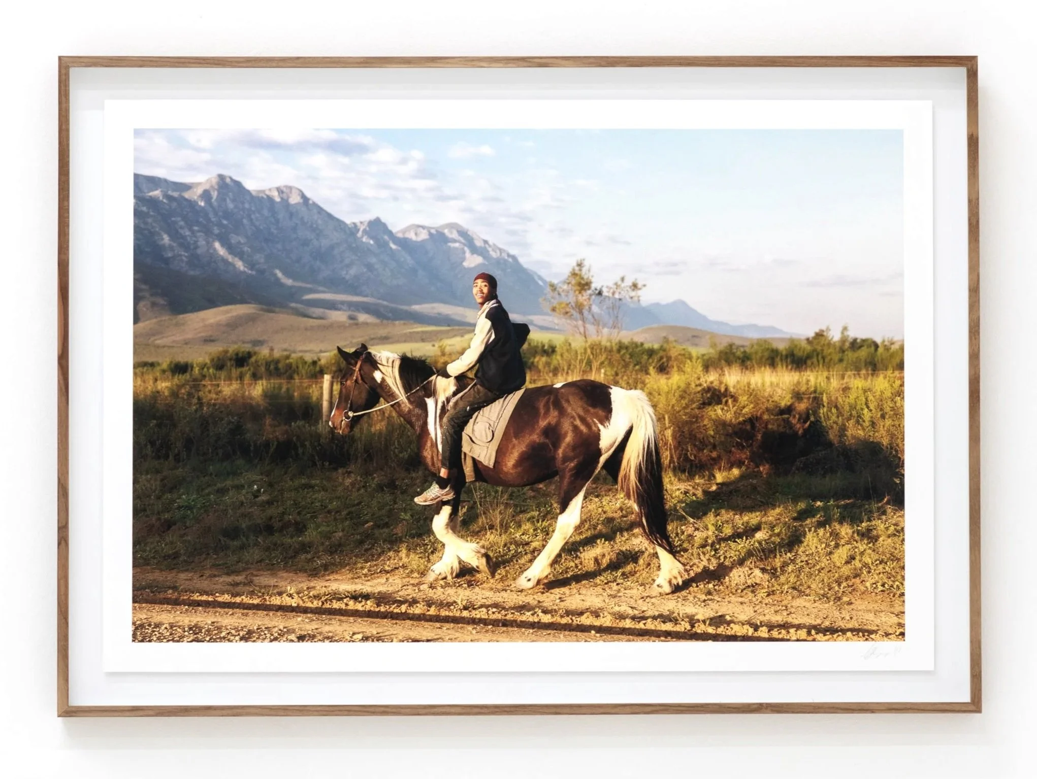 A framed photograph of a person riding a horse in a scenic outdoor setting with mountains in the background.