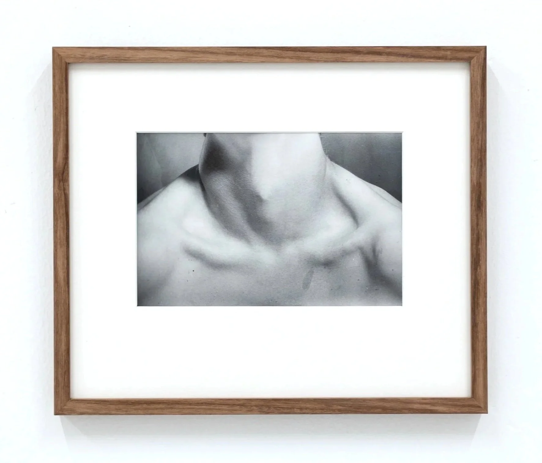Black and white photograph of a person's neck and shoulders framed in a wooden frame, hung on a white wall.