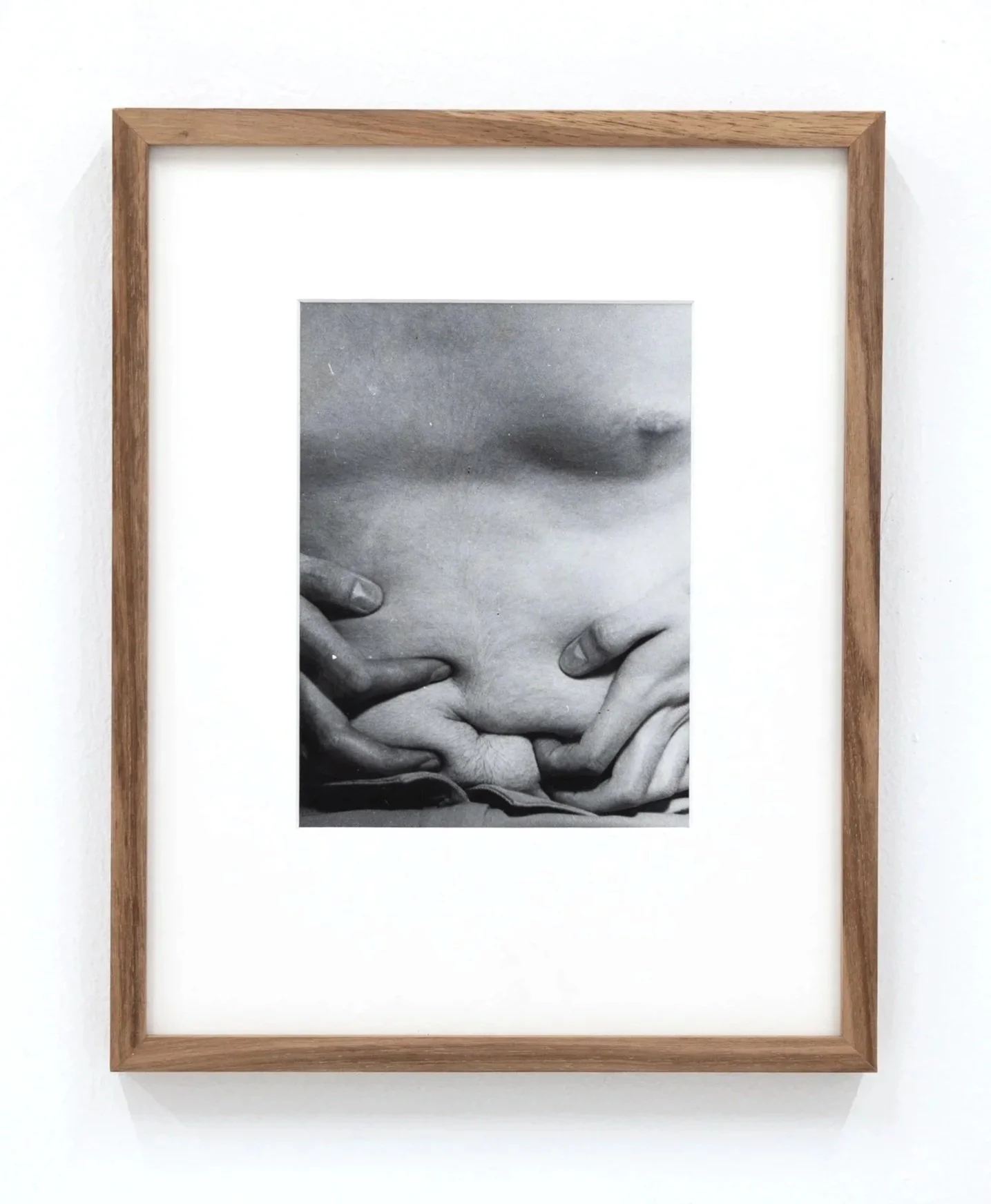 Black and white photograph of two hands gently touching, framed in a wooden border hung on a white wall.