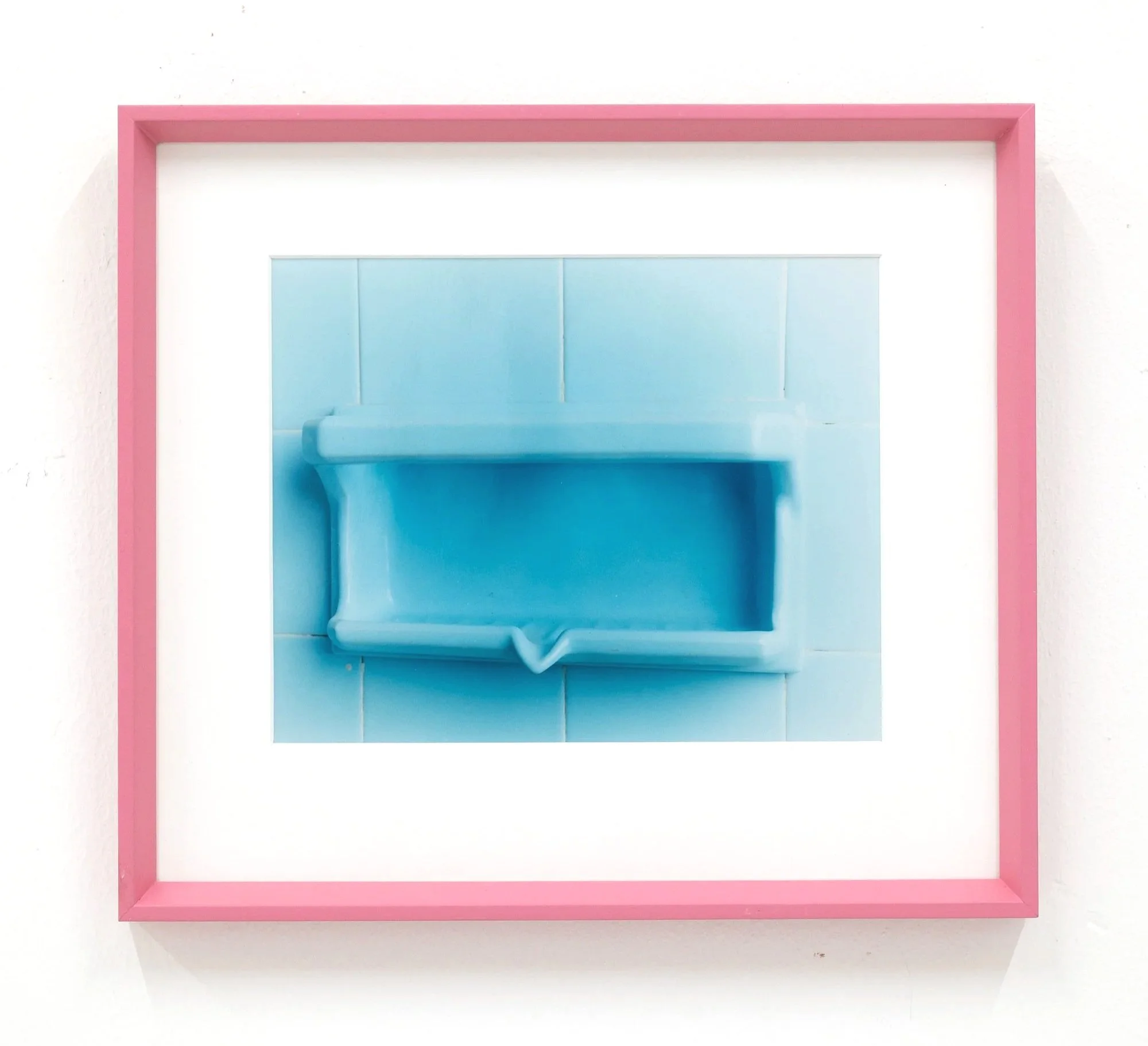 Close-up of a pink picture frame on a white wall, with a reflection of a blue arch or door and part of a ceiling.