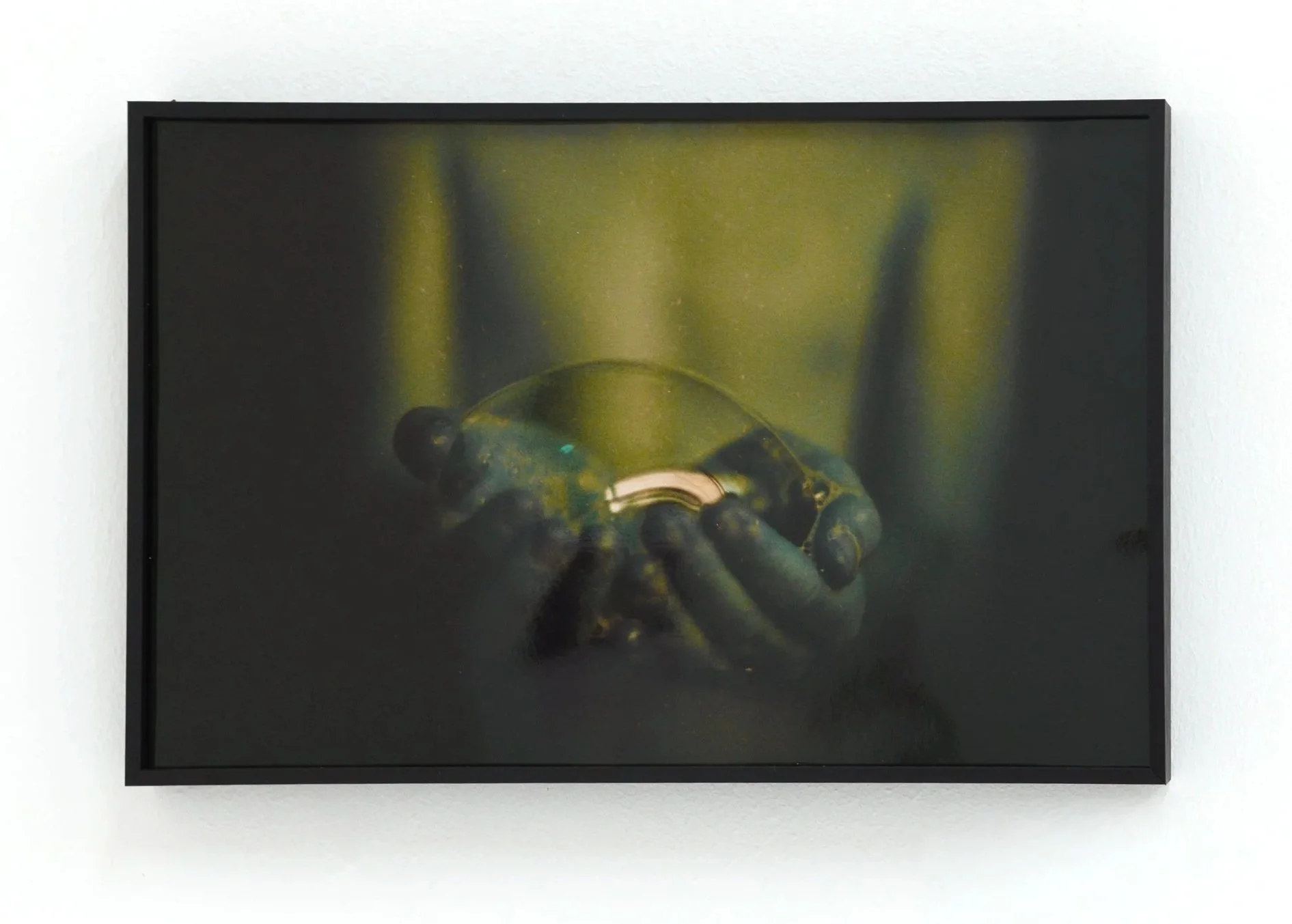 Framed artwork of a close-up hand holding a small object, possibly a glass or a metallic item.