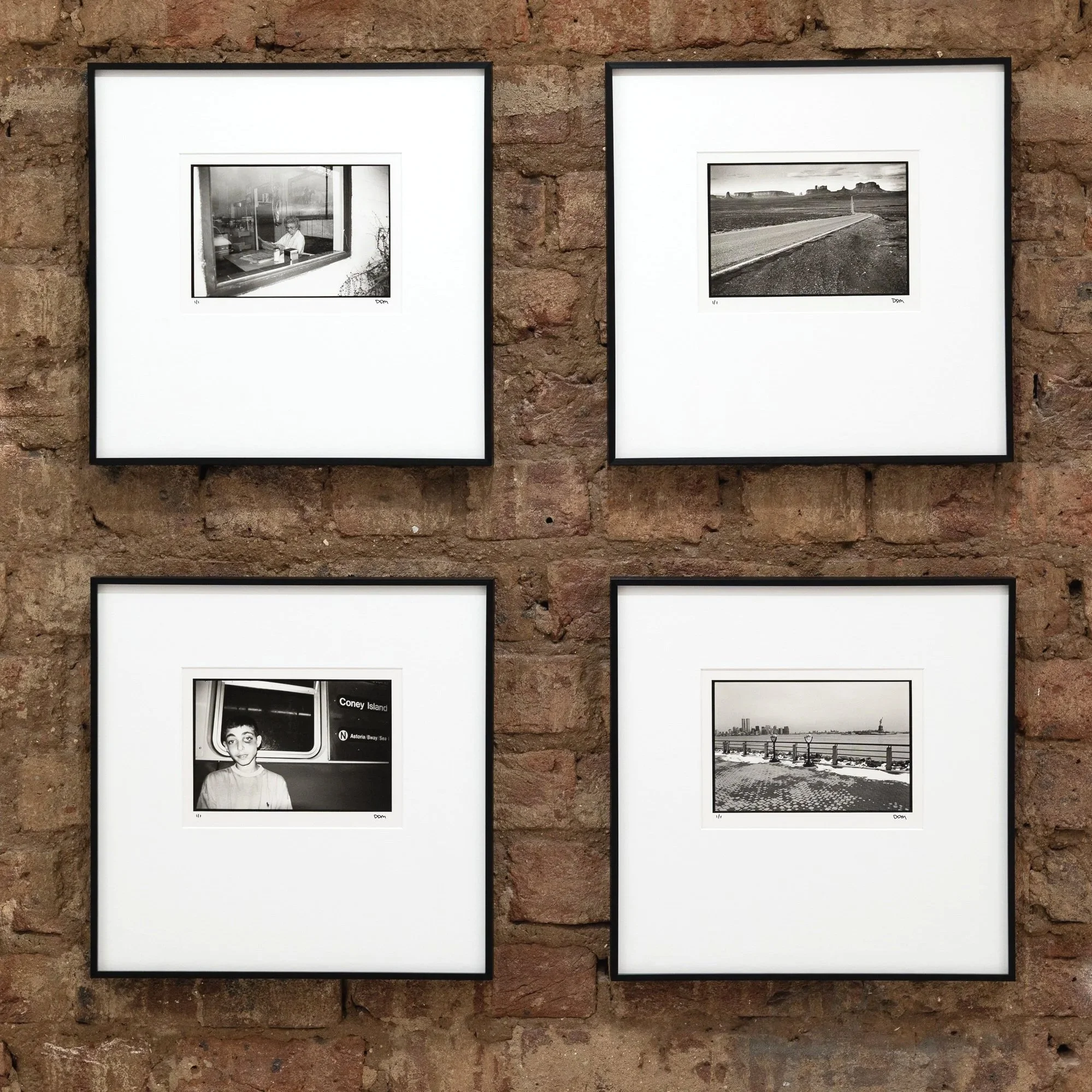 Set of four black-and-white photographs framed and hung on a brick wall.