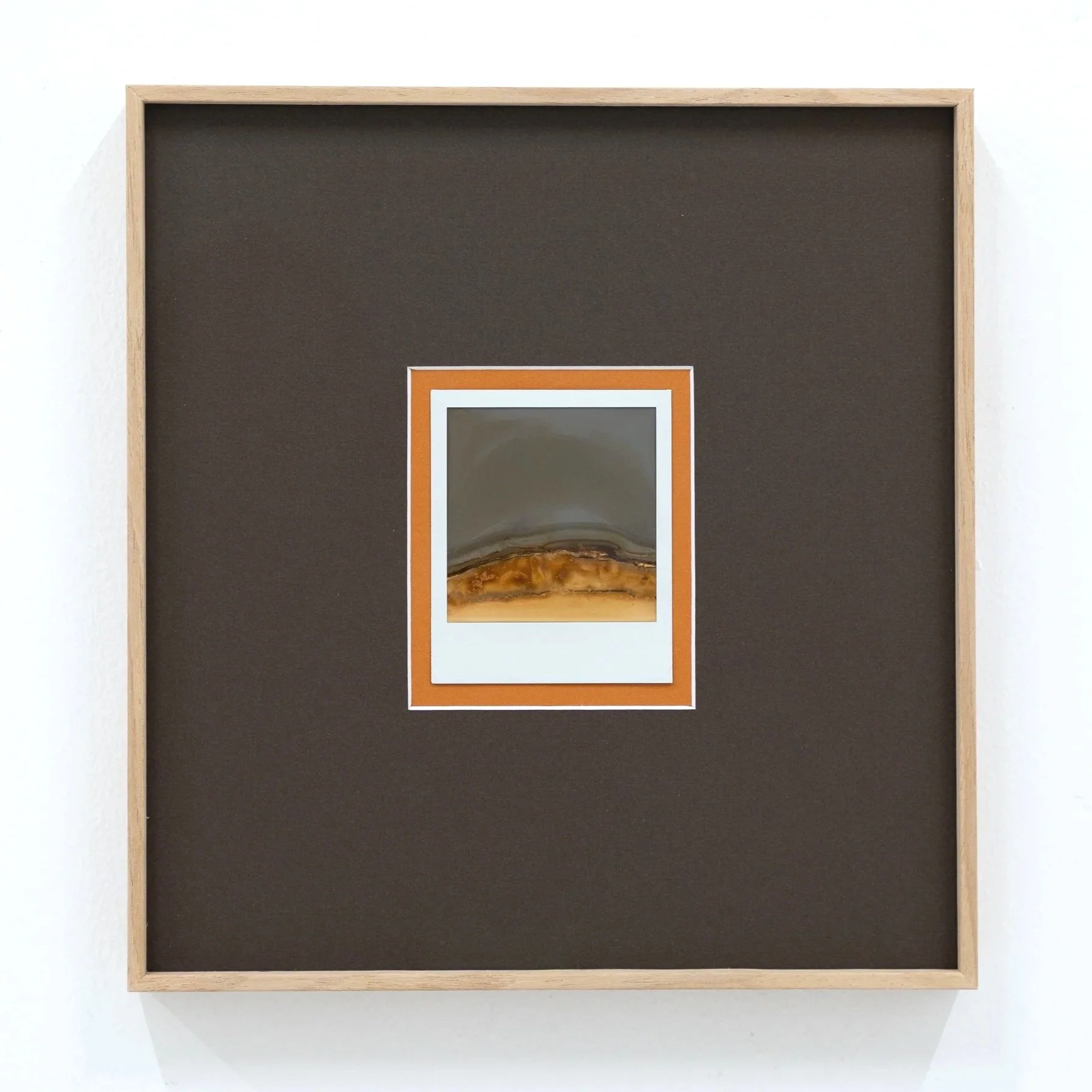 A framed picture with an orange border, placed on a white wall, featuring a landscape with a mountain and desert scene.