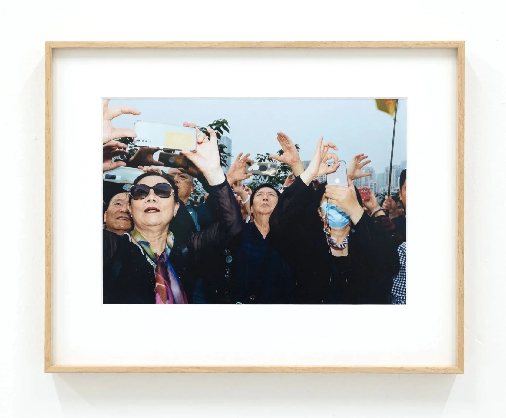 Photograph of a group of people taking selfies outdoors, with urban skyline in the background.
