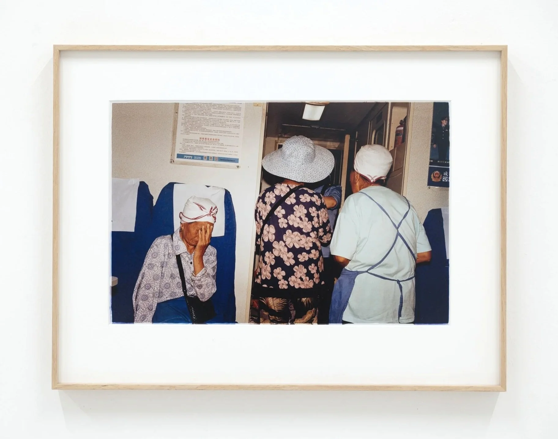A framed photograph of elderly women in a waiting area, with one woman covering her face, and others wearing hats and engaging in conversation.