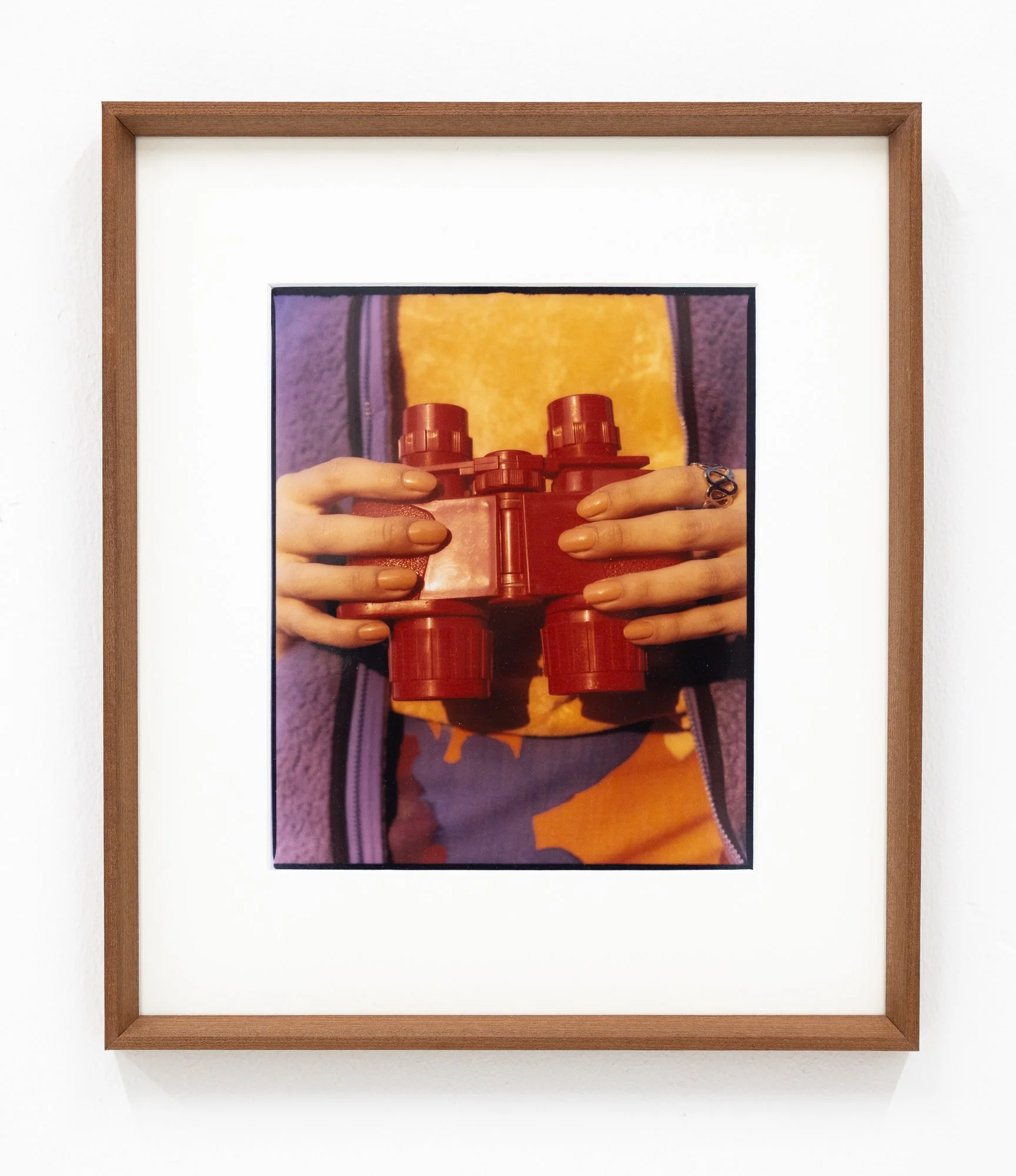 Photograph of a framed artwork on a white wall showing hands holding a cluster of red soda bottles.