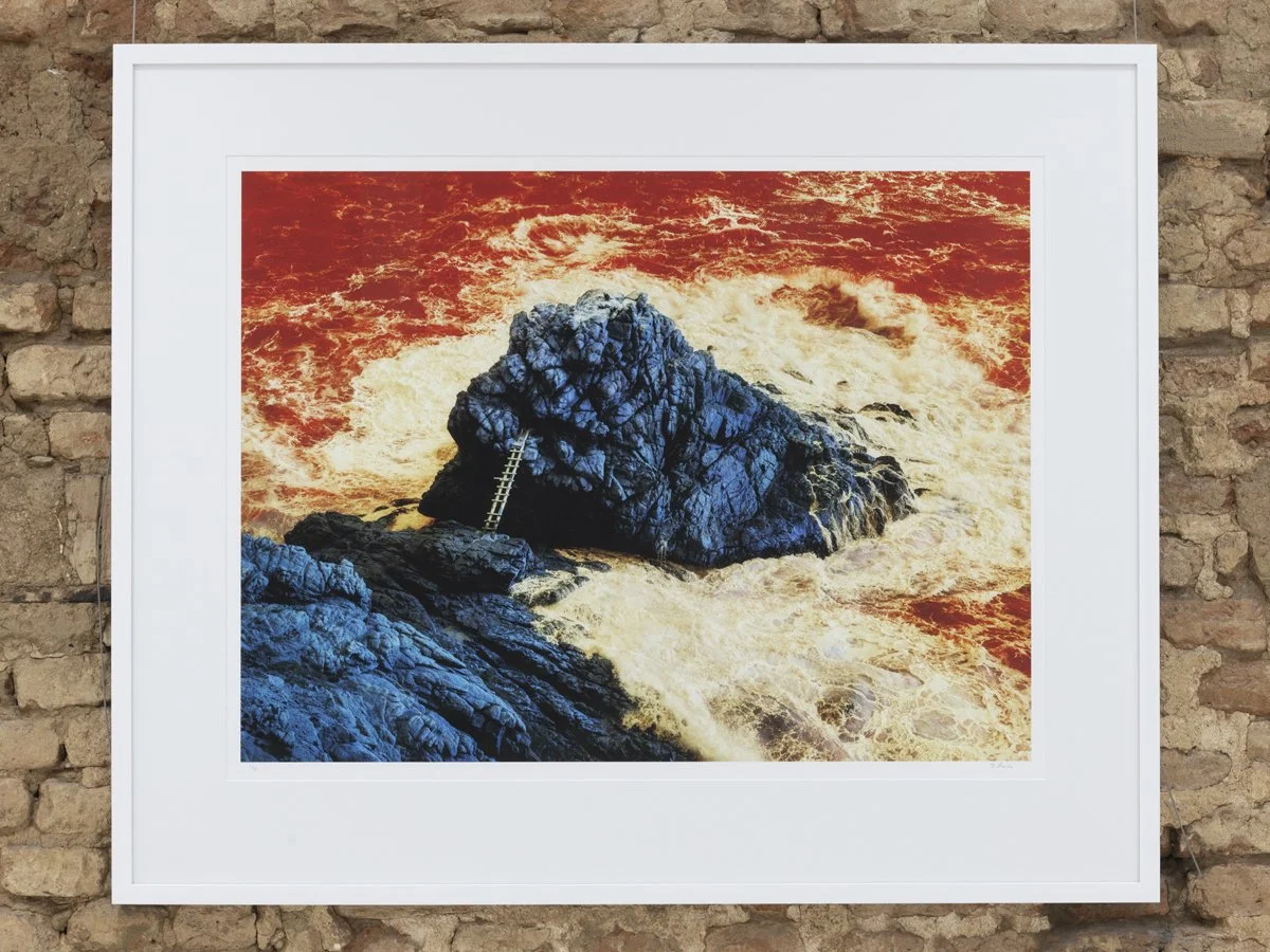 Artwork of a large dark rock formation in turbulent ocean water with a ladder leaning against the rock, all under a fiery orange sky.