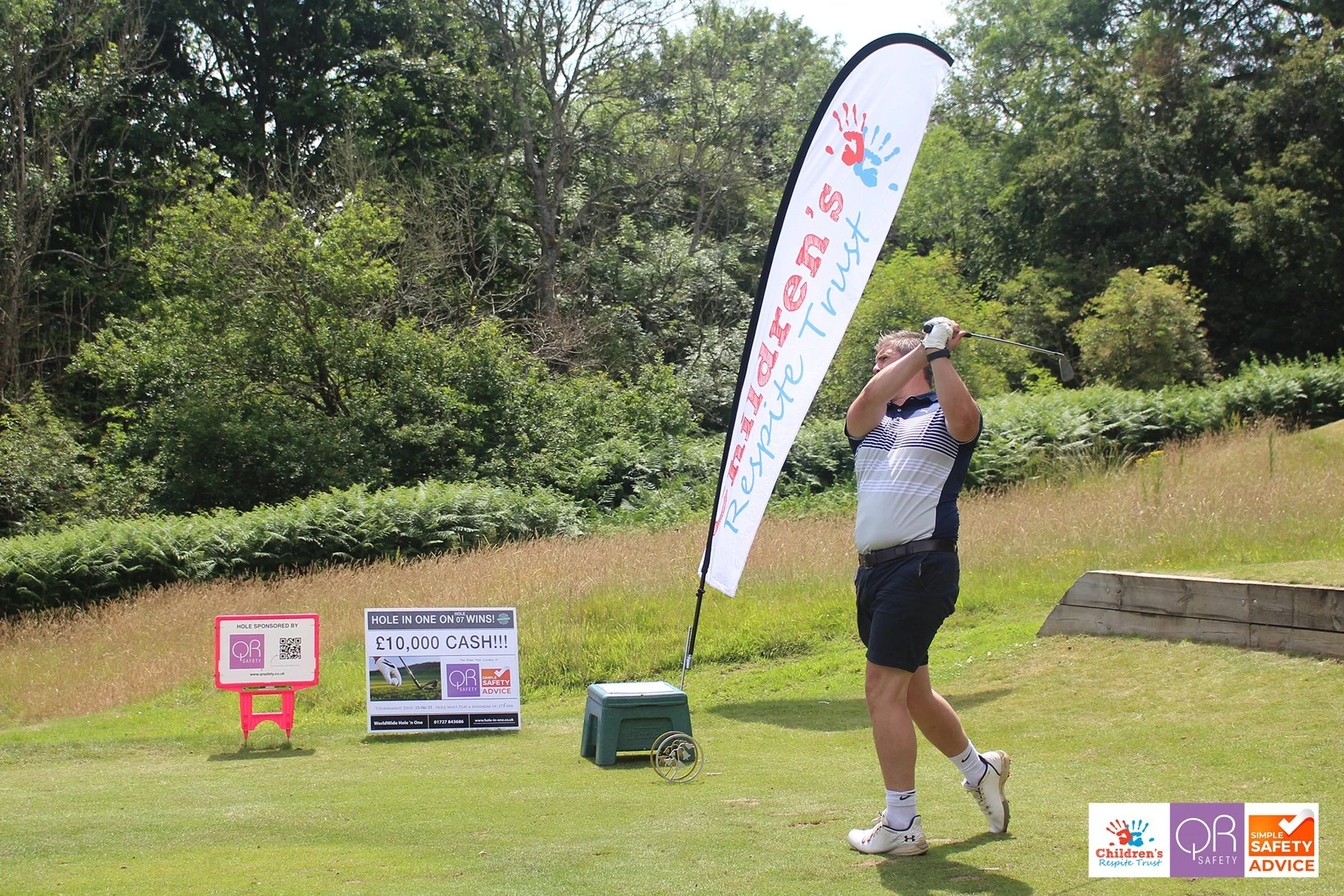 A man playing golf on a course, swinging a club. There is a flag with 
