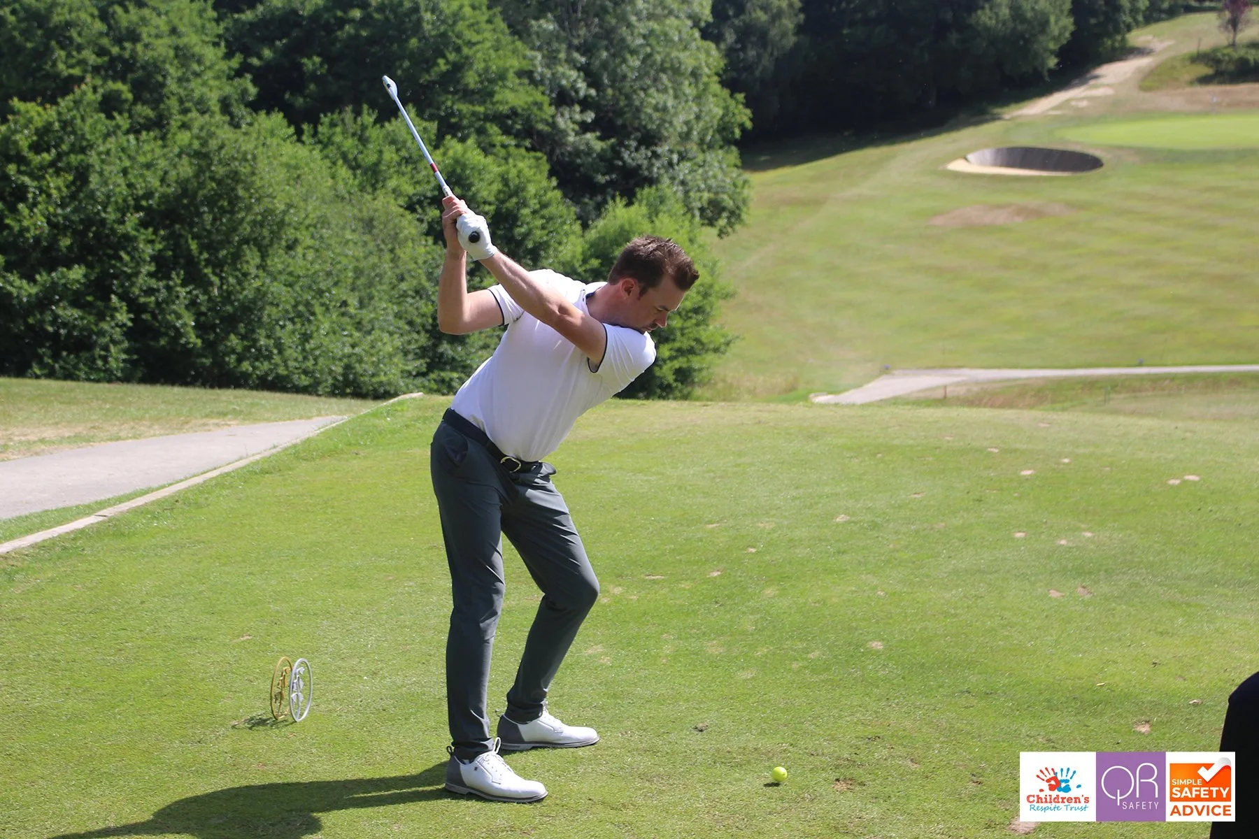 A man hitting a golf ball on a golf course with a wooded area in the background.