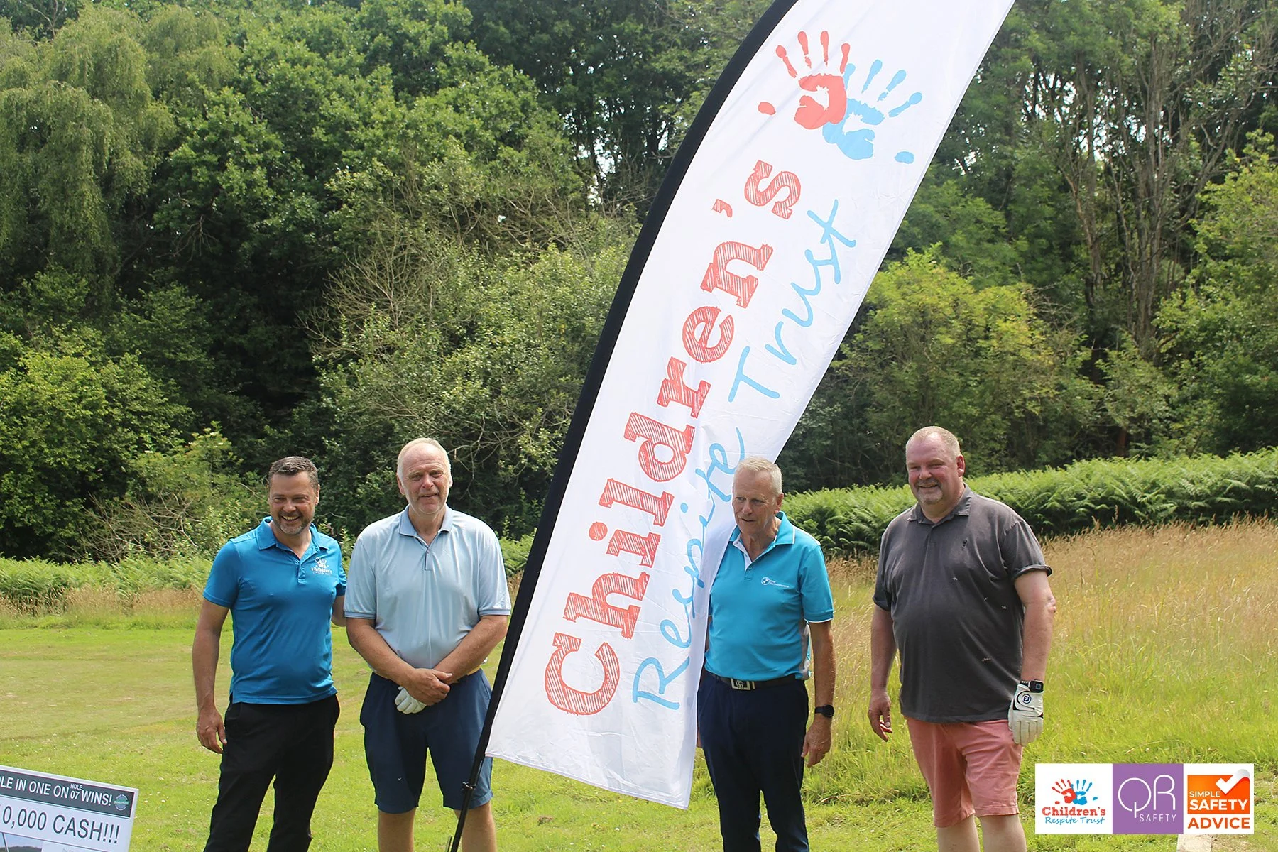 Four men standing on a golf course, next to a large vertical banner that reads 'Children's Response Trust' with colorful handprints. The men are smiling and dressed in casual golf attire. The background shows lush green trees and grass.