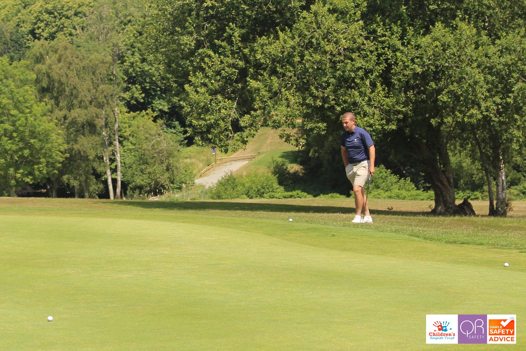A man playing golf on a green course surrounded by trees.