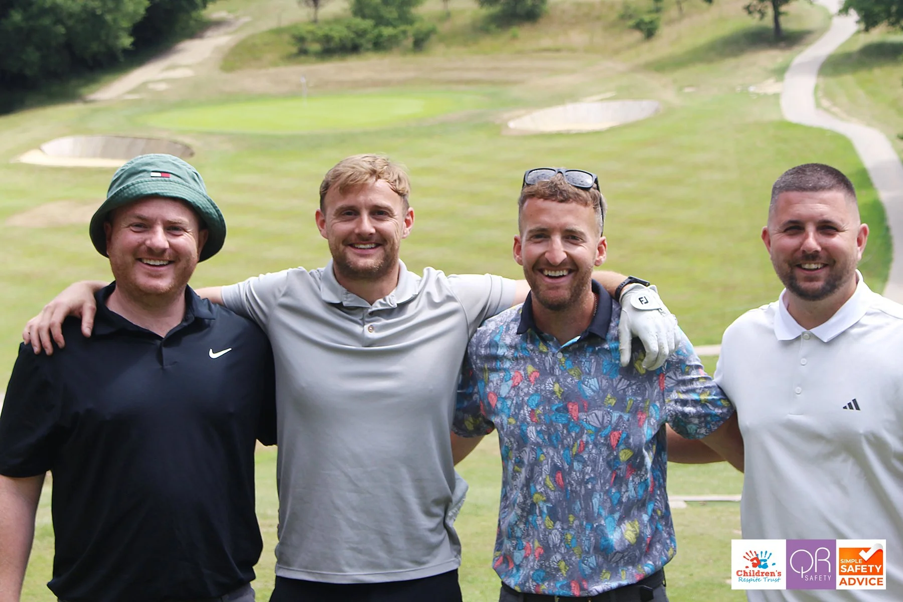 Four men standing on a golf course, smiling with their arms around each other