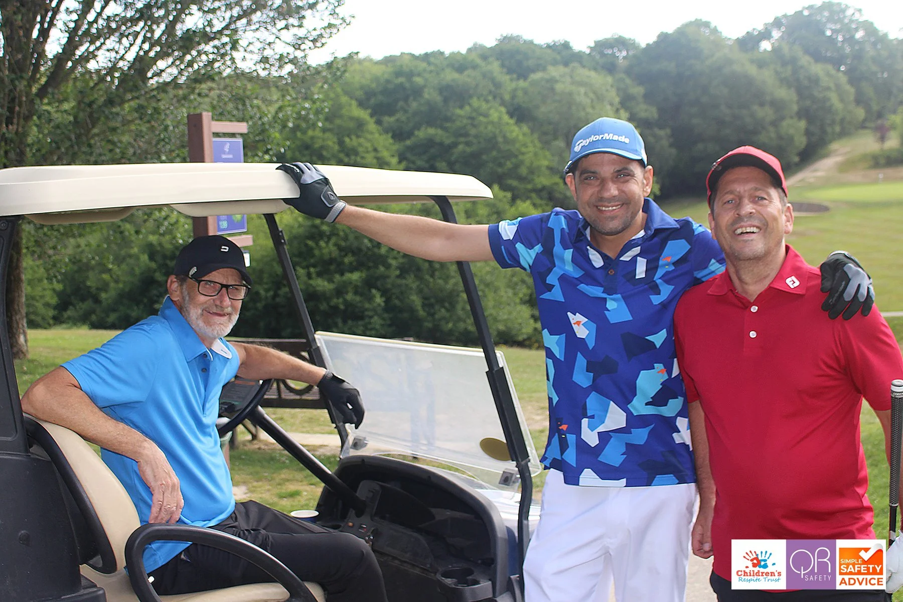 Three men posing with golf clubs next to a golf cart on a golf course, lush greenery in the background, smiling