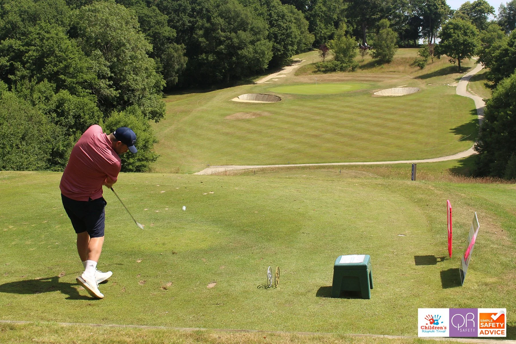 Man taking a golf shot on a golf course with trees and sand bunkers in the background.