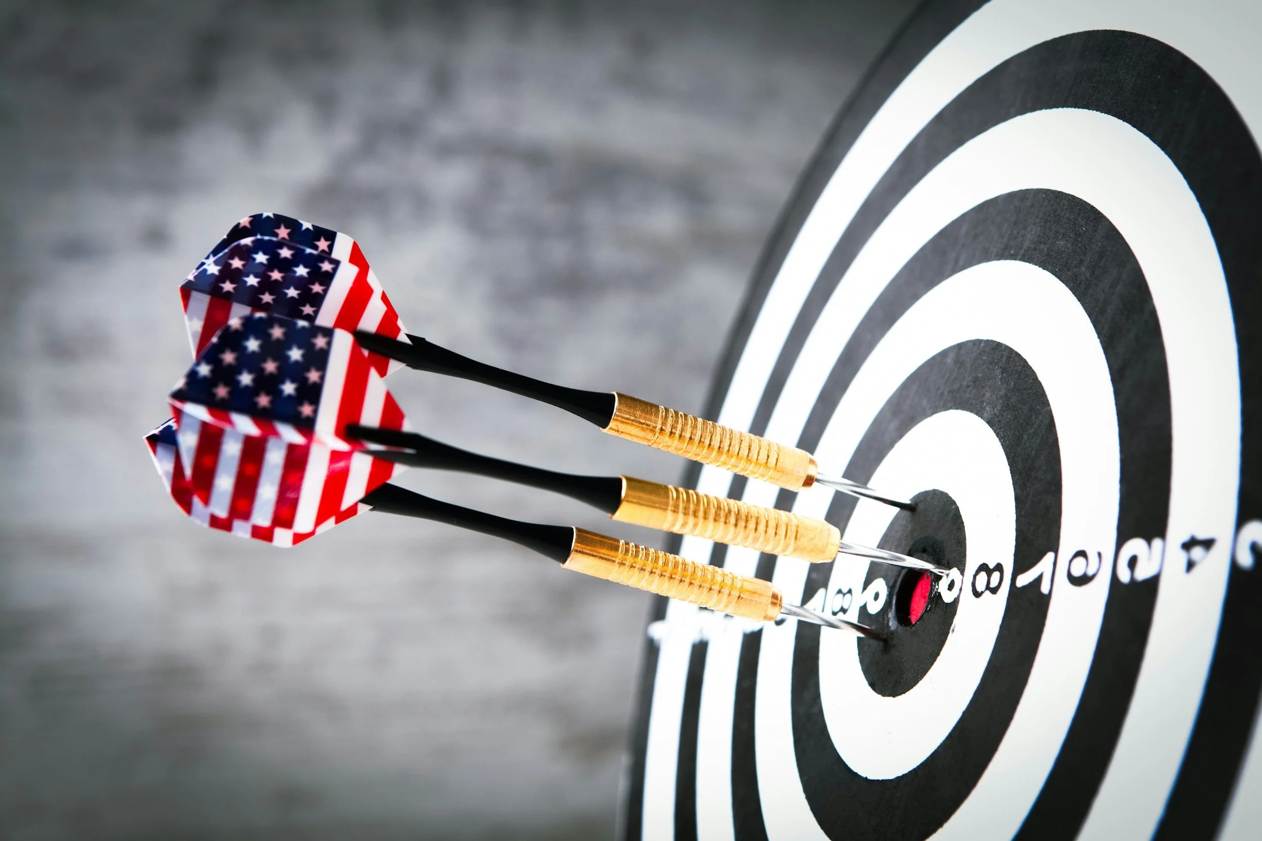 Three darts with American flag pattern stuck in the bullseye of a black and white target.