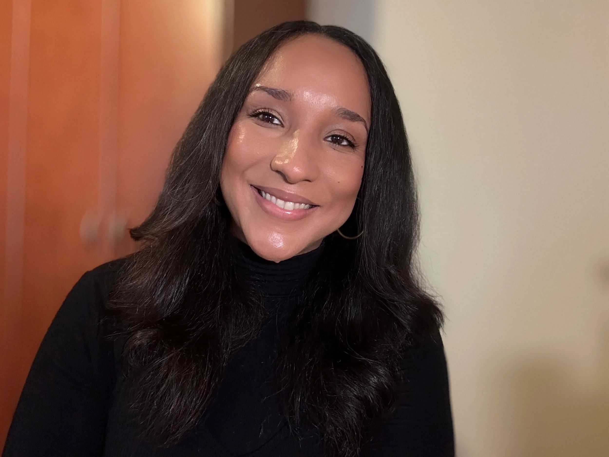 A smiling woman with long, dark hair wearing a black turtleneck.