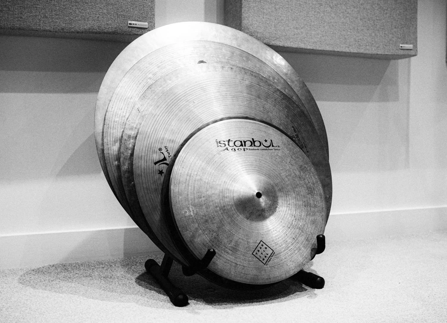 A set of three cymbals on a stand placed on a light-colored floor against a plain wall, with a speaker in the background.