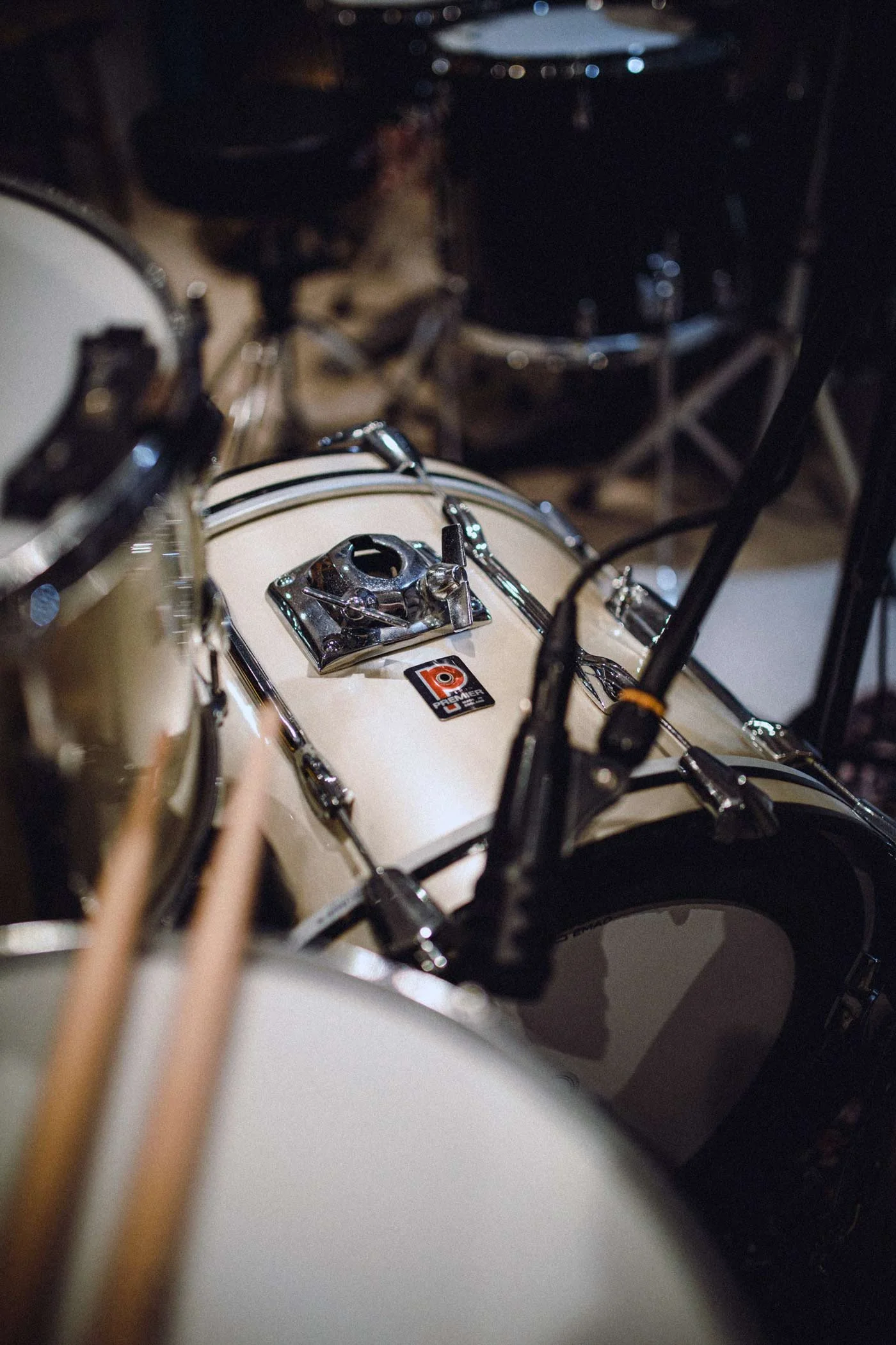 Close-up of a drum set with a beige bass drum, metallic tension rods, and black cymbals in a dimly lit setting.