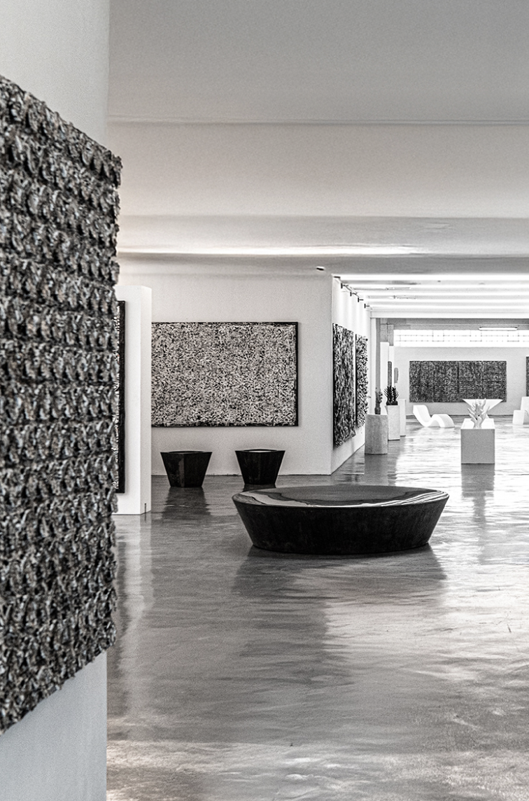Interior of an art gallery or museum with abstract artwork on white walls, modern sculptures, and seating arrangements.