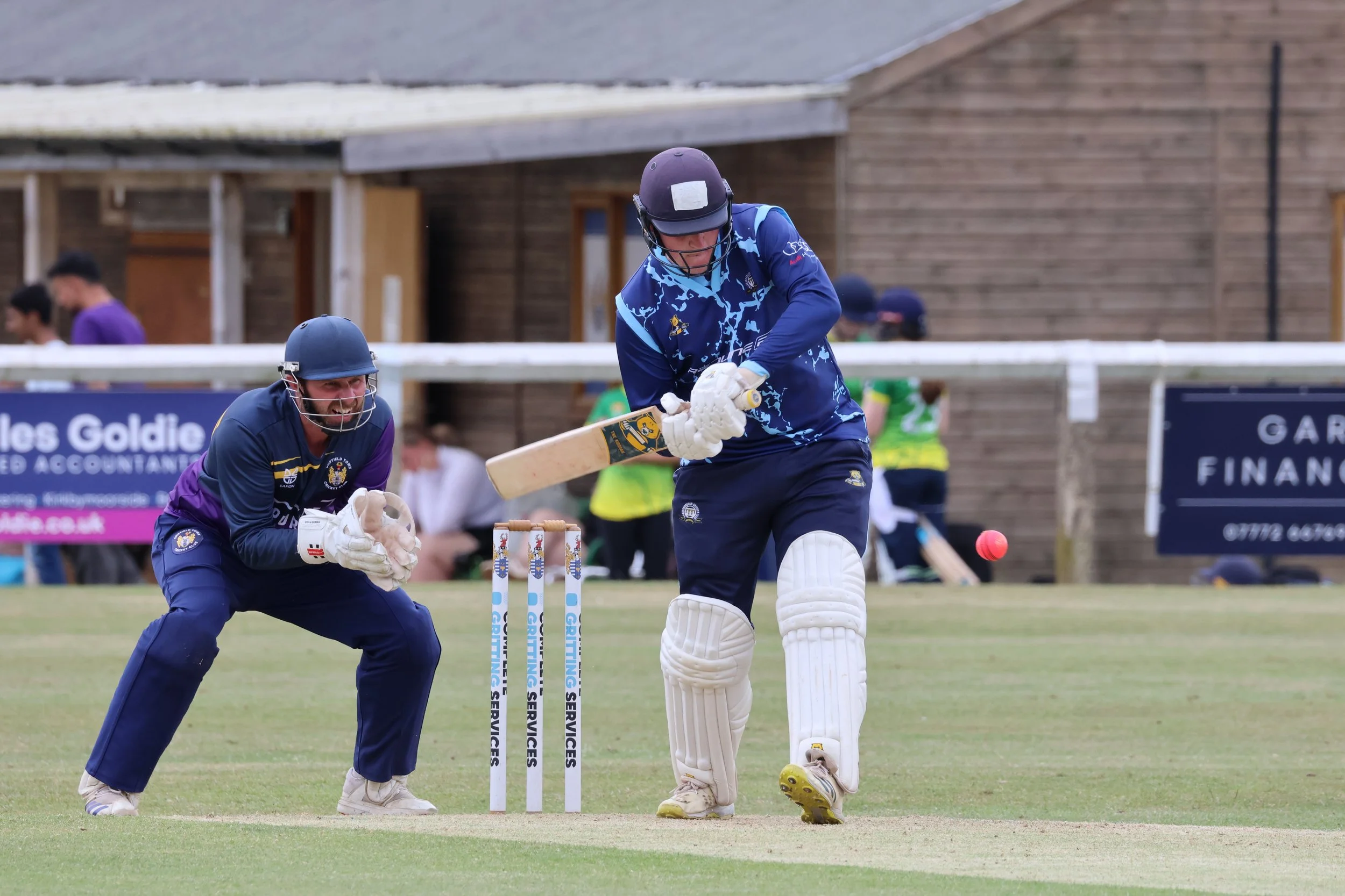 Cricket players celebrating during a match on the field with a wooden building in the background.