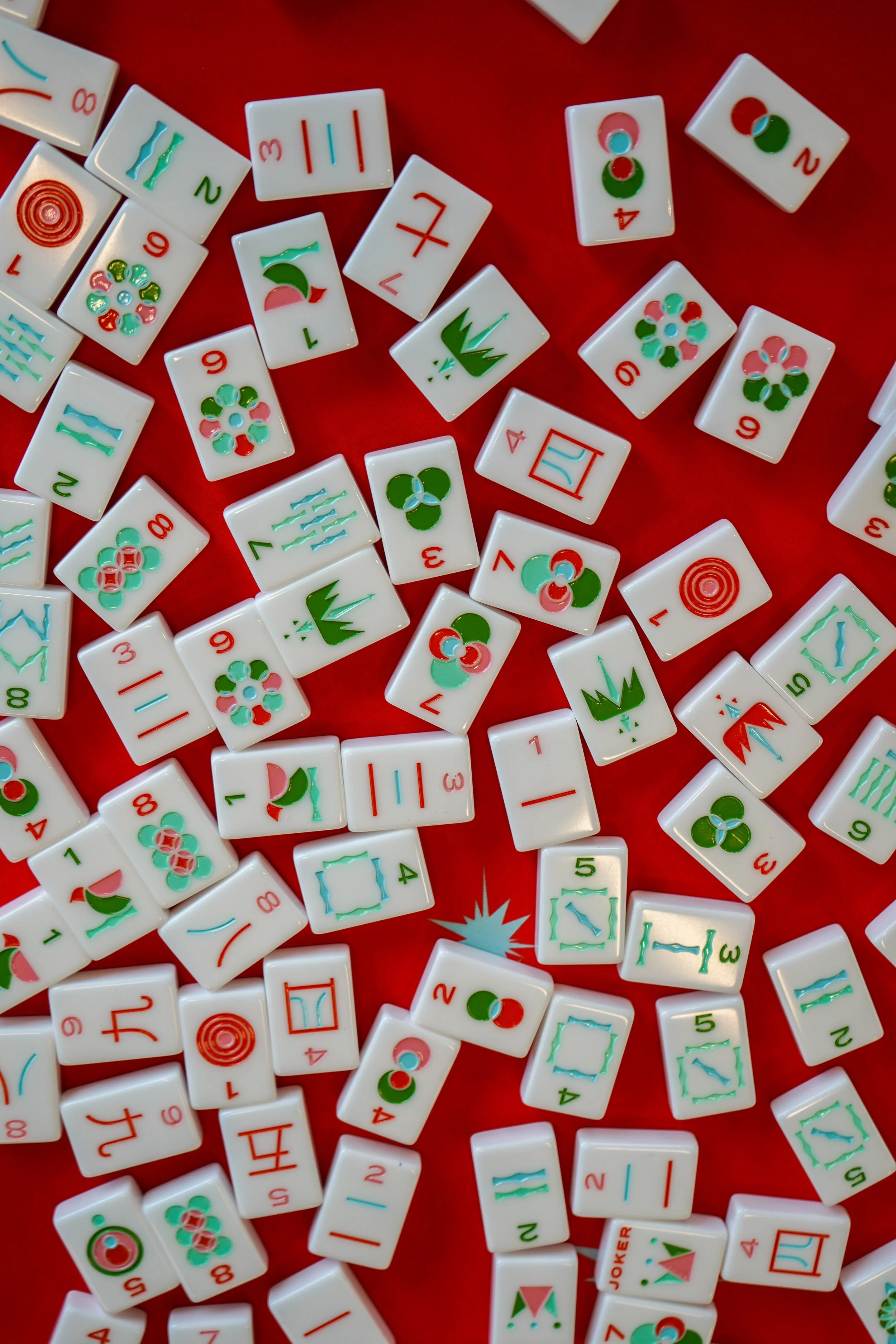Scattered Mahjong tiles with various symbols and red, green, pink, and blue colors on a red background.