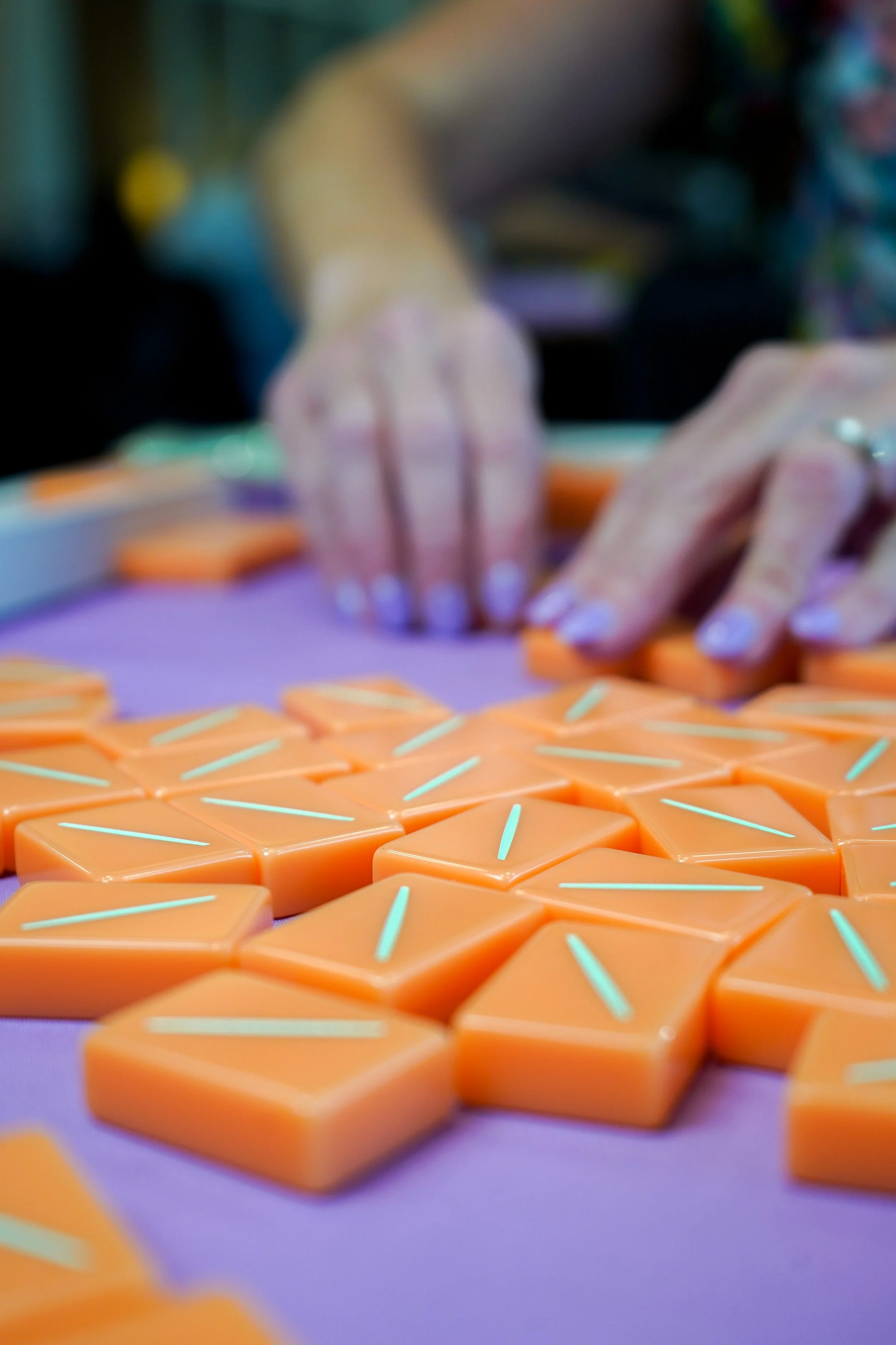 Close-up of orange hexagonal tiles with glowing white lines, arranged in a pattern, with hands in the background playing a game.