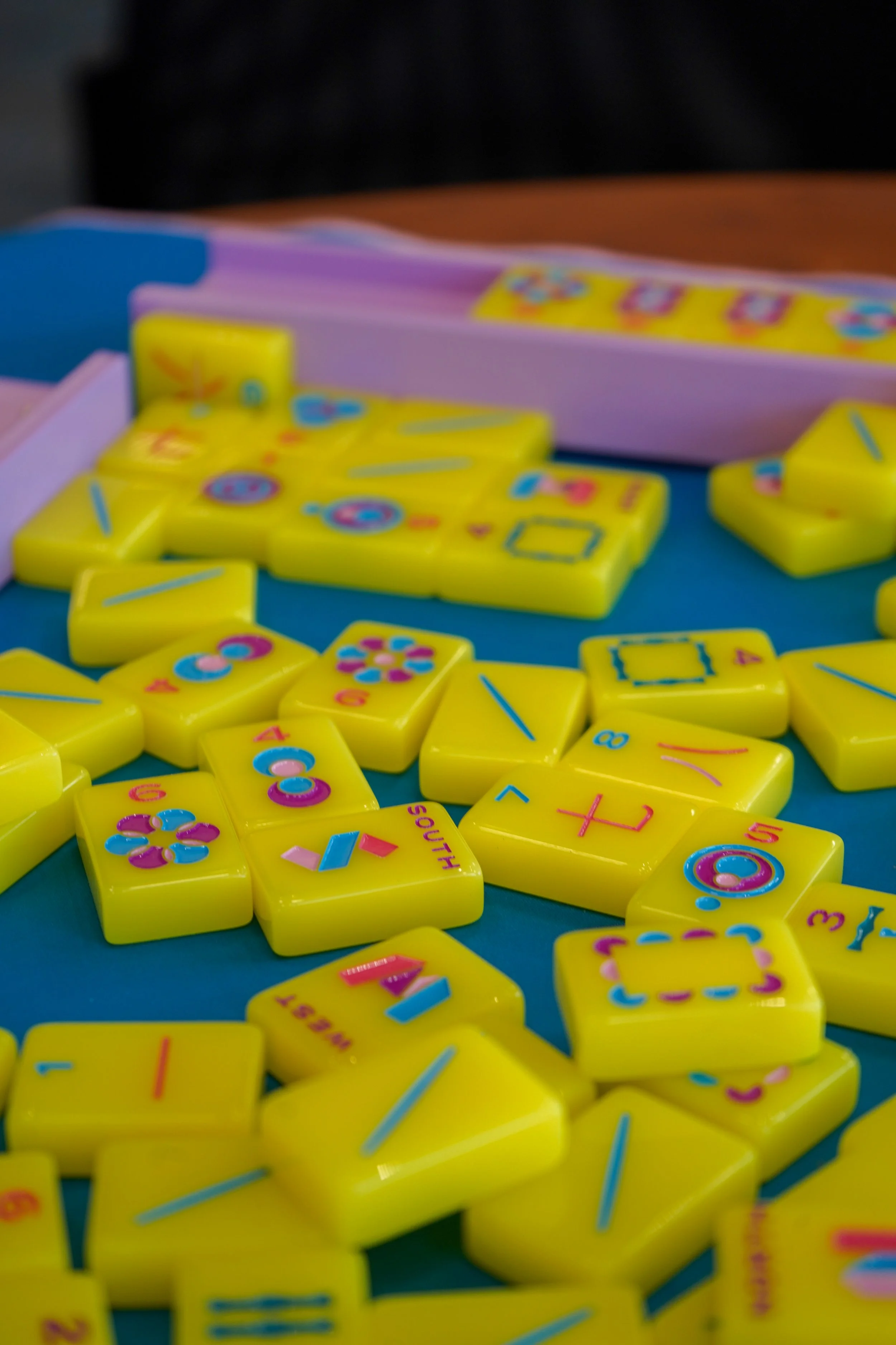 Close-up of yellow Mahjong tiles with colorful symbols and characters, scattered on a surface.