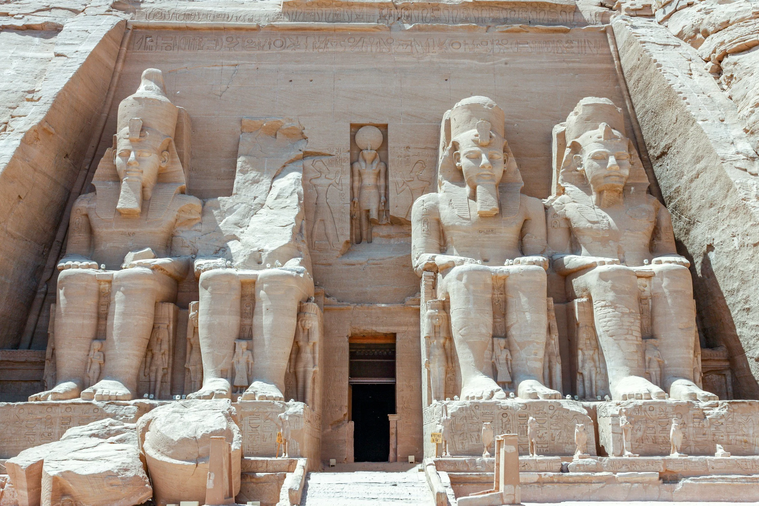 Ancient Egyptian temple with large carved statues of pharaohs at the entrance, surrounded by hieroglyphic inscriptions on the stone facade.
