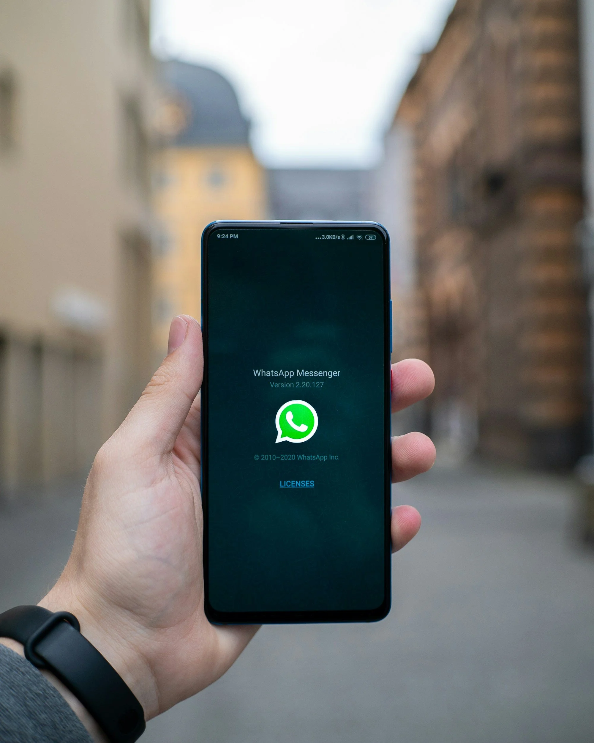 Person holding a smartphone displaying the WhatsApp Messenger app with a blurred outdoor background.