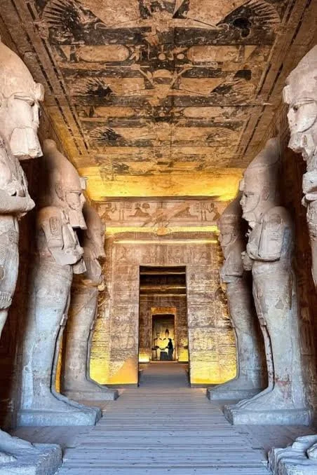 Ancient Egyptian temple hallway with large statues of pharaohs and hieroglyphic carvings on the walls and ceiling.